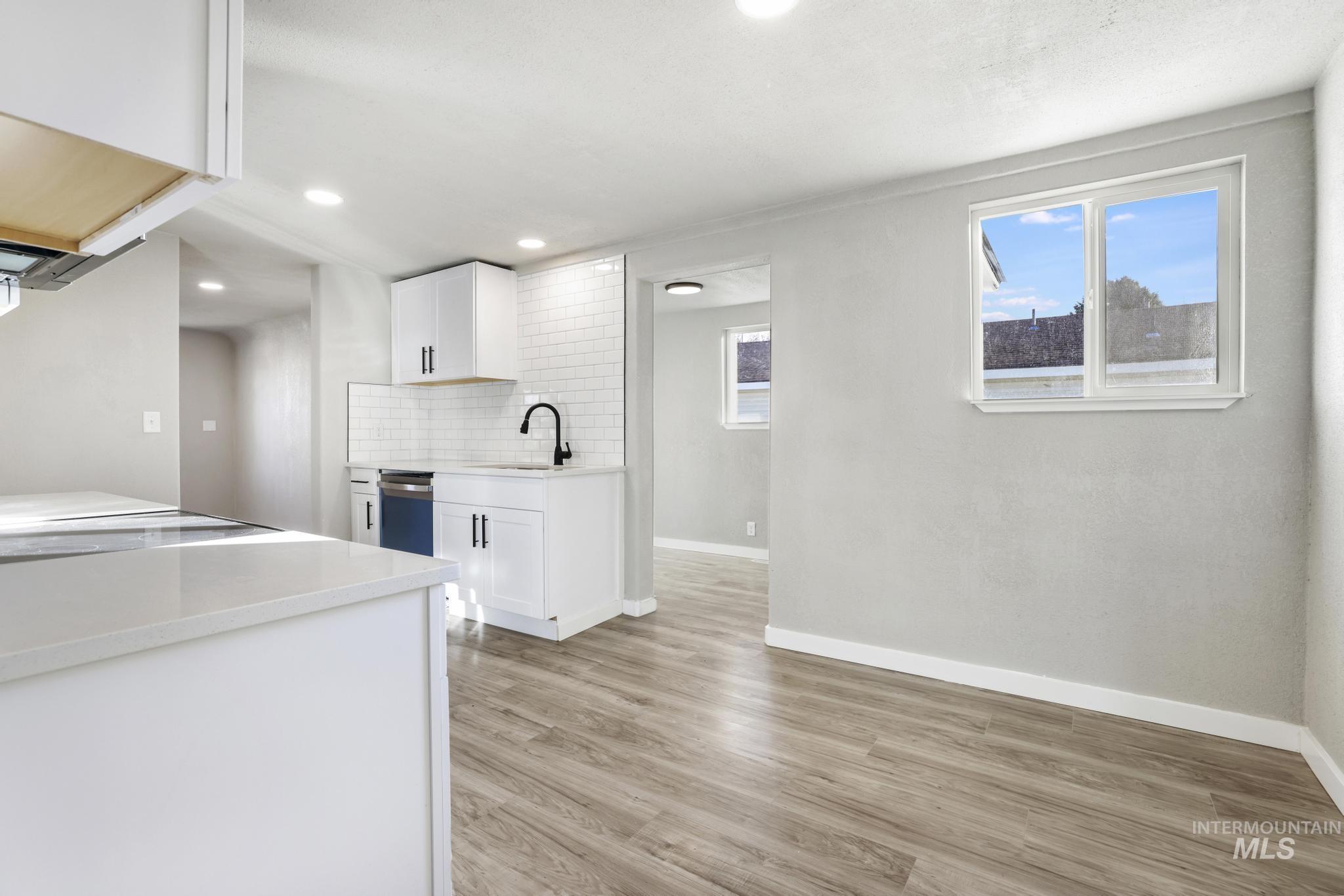 Kitchen with white cabinets, decorative backsplash, light wood-type flooring, light stone counters, and recessed lighting
