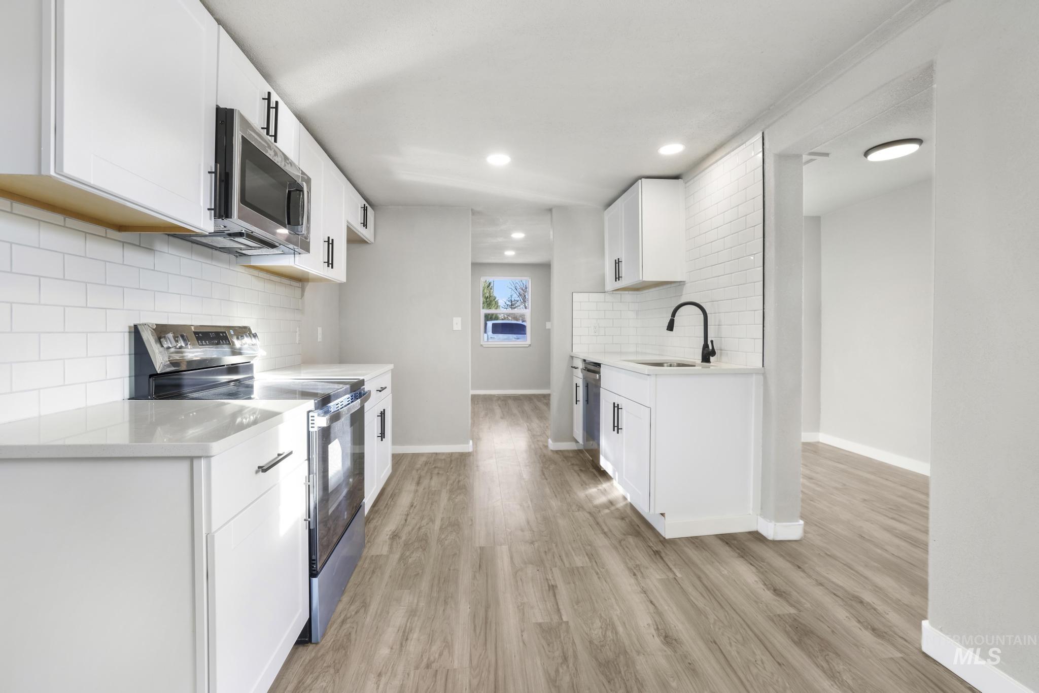 Kitchen with appliances with stainless steel finishes, white cabinetry, light stone countertops, light wood finished floors, and recessed lighting