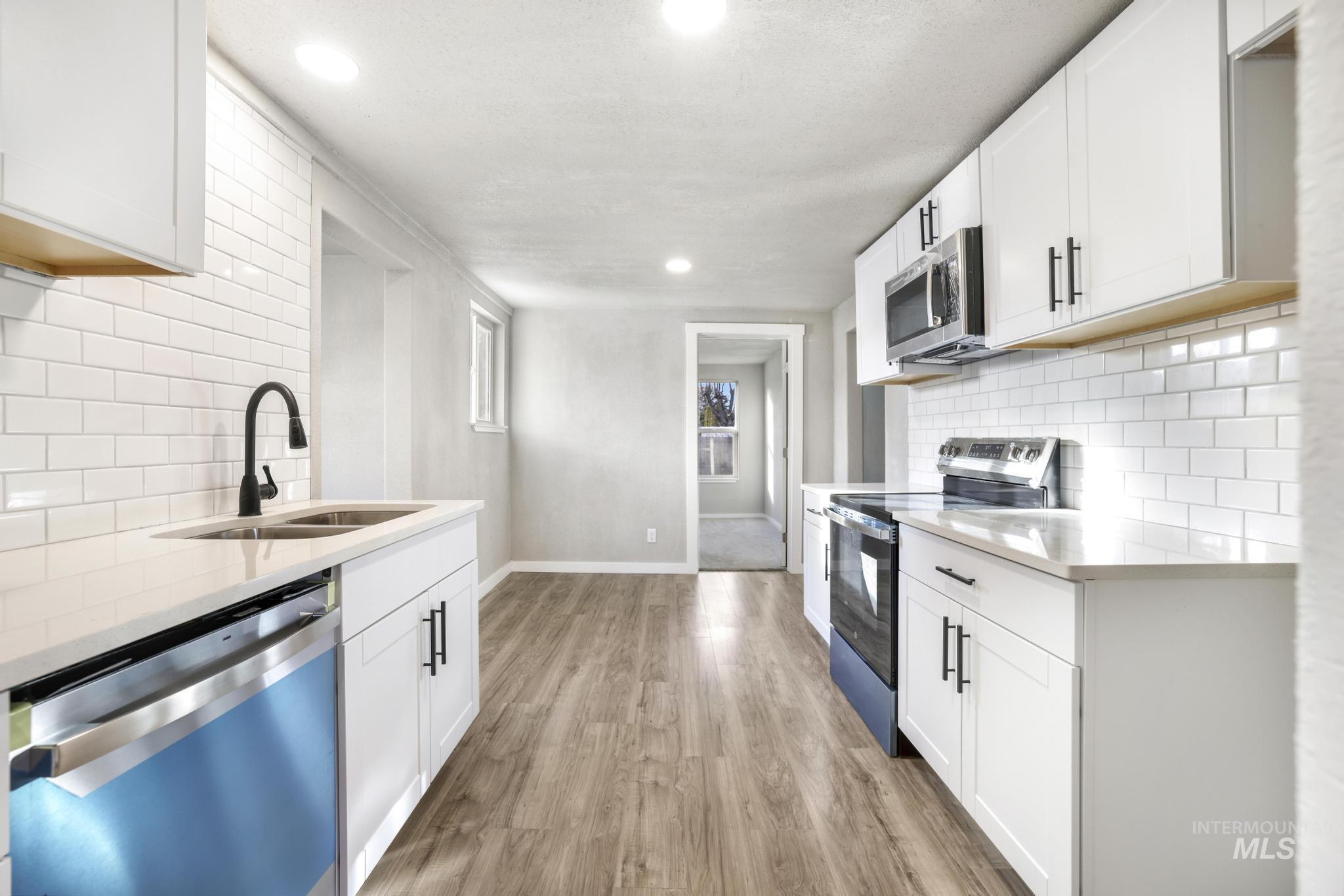 Kitchen with backsplash, appliances with stainless steel finishes, white cabinetry, and recessed lighting