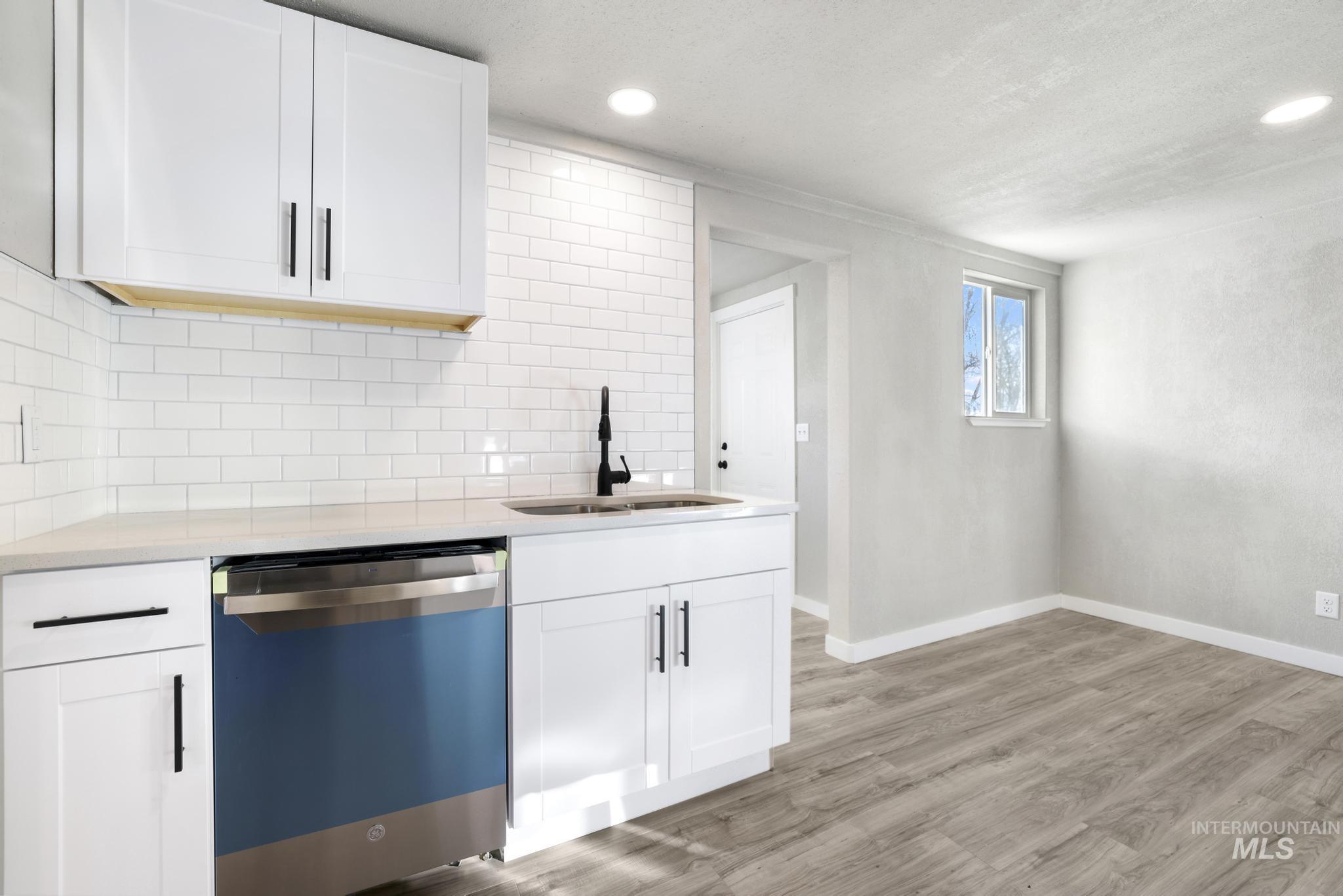 Kitchen with dishwashing machine, white cabinetry, decorative backsplash, light stone countertops, and light wood-style floors