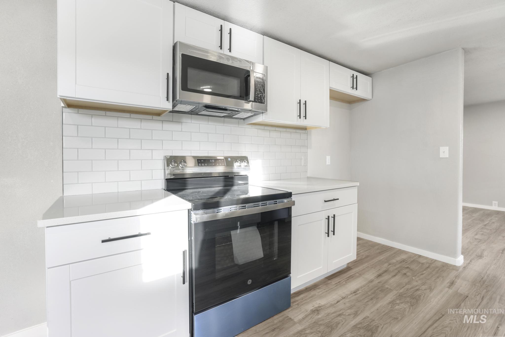 Kitchen featuring appliances with stainless steel finishes, white cabinetry, tasteful backsplash, light wood-type flooring, and light stone countertops