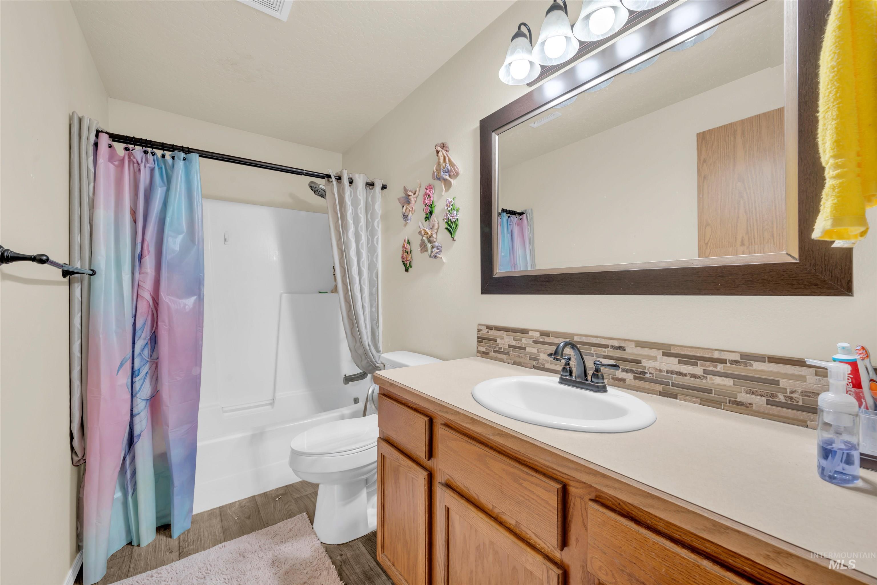 Bathroom with shower / bath combo with shower curtain, dark wood-style floors, vanity, and backsplash
