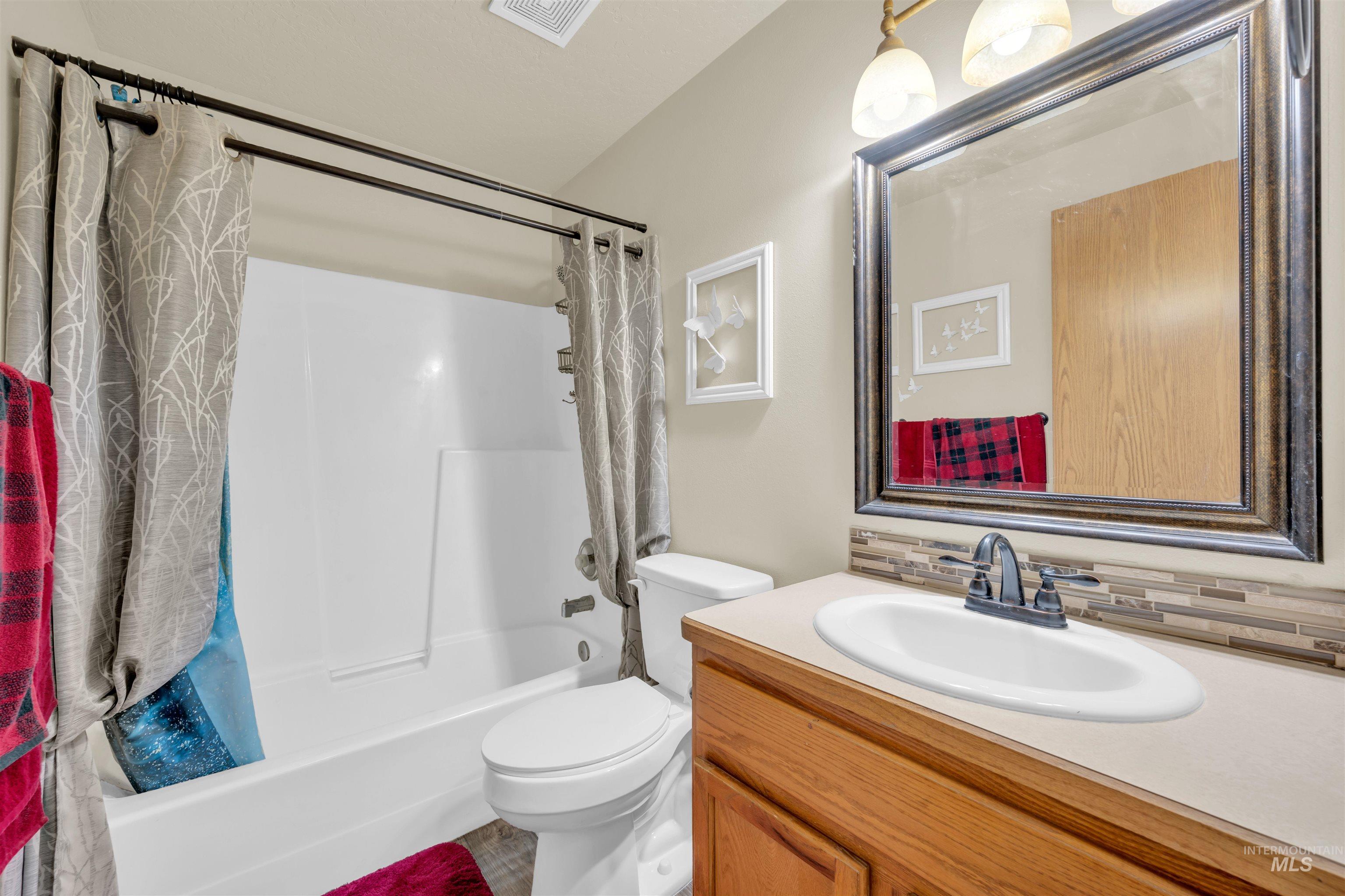 Bathroom featuring shower / bathtub combination with curtain, vanity, and tasteful backsplash