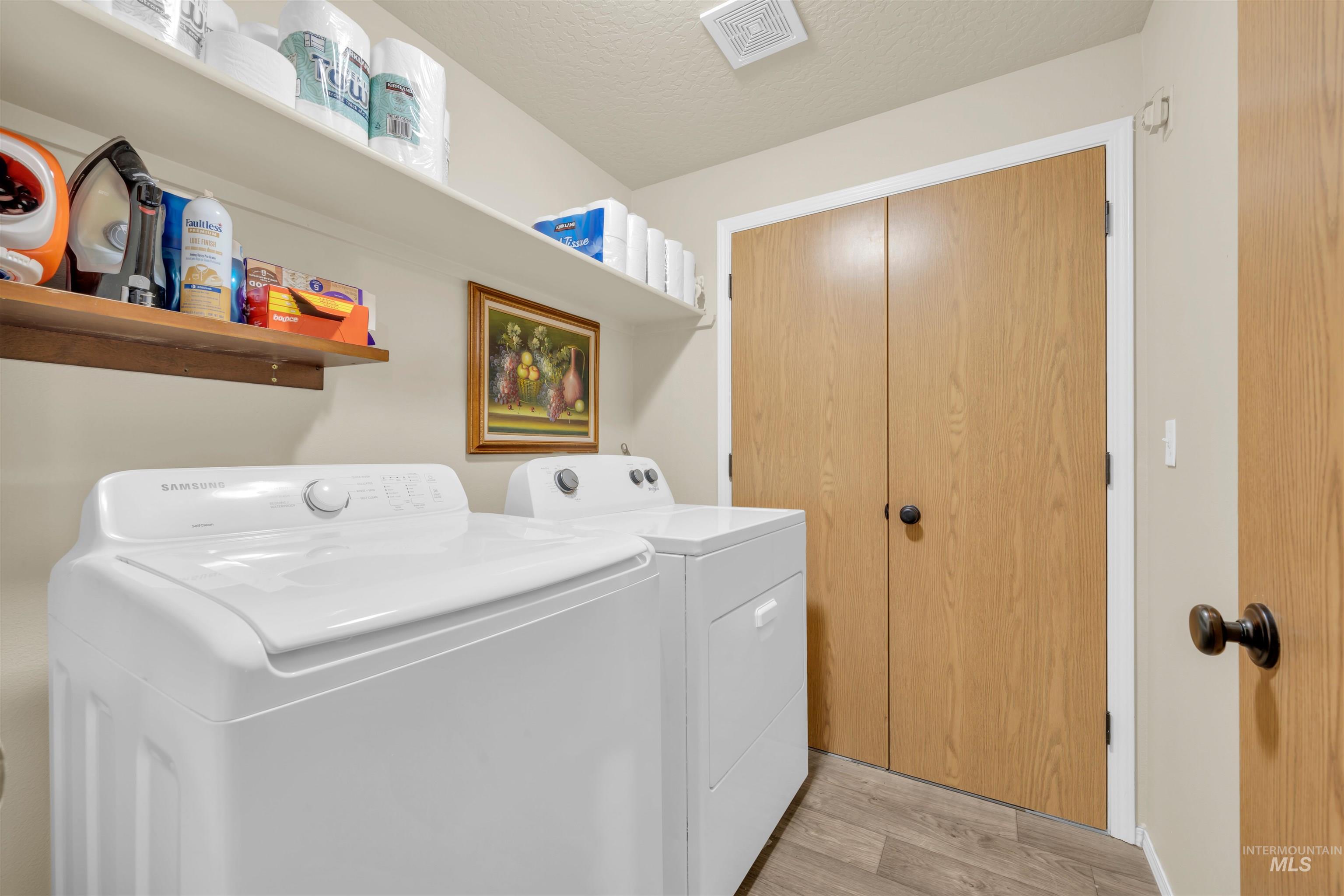 Washroom with separate washer and dryer, a textured ceiling, and light wood finished floors