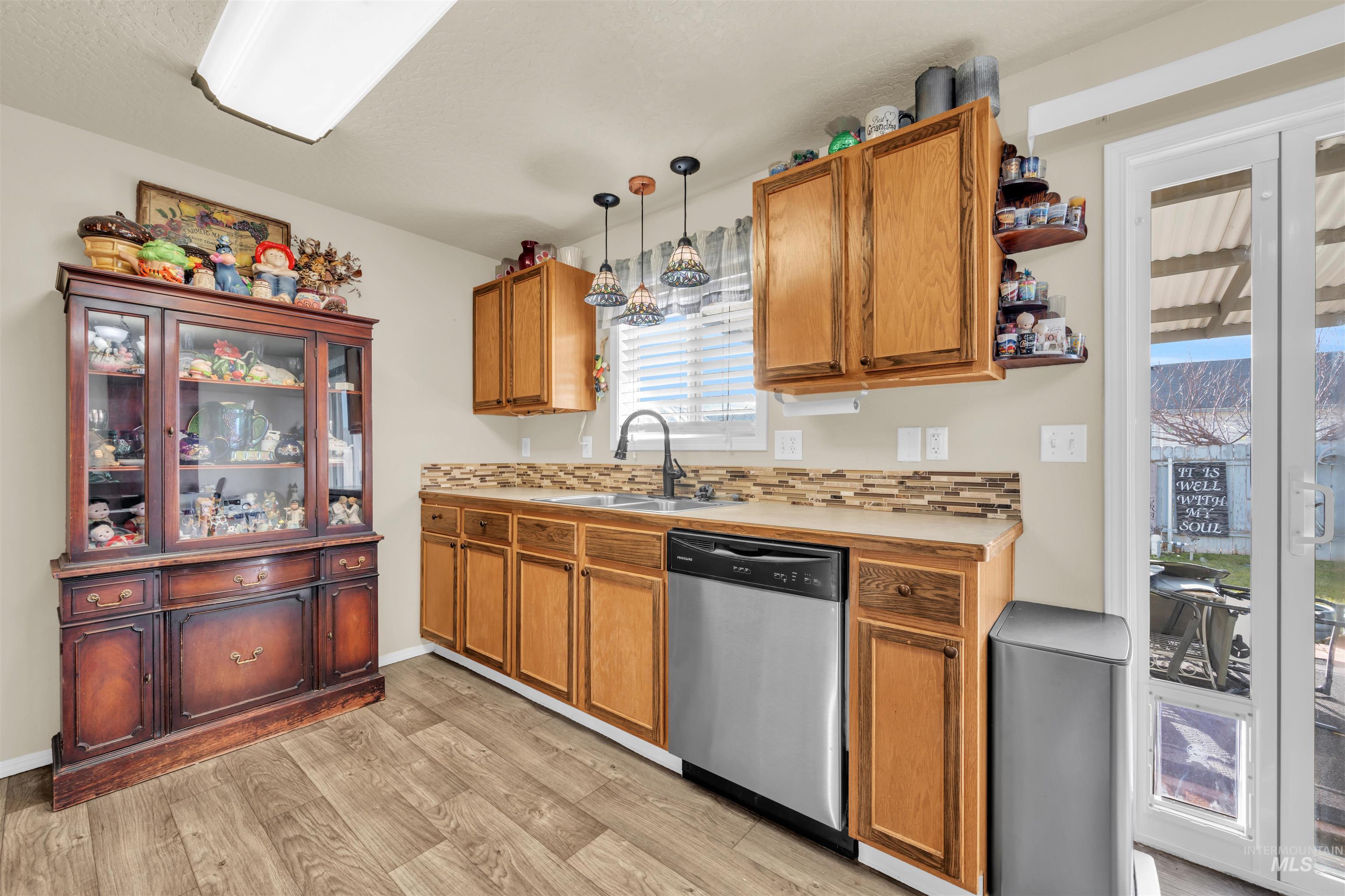 Kitchen featuring light countertops, decorative light fixtures, decorative backsplash, stainless steel dishwasher, and light wood-style floors