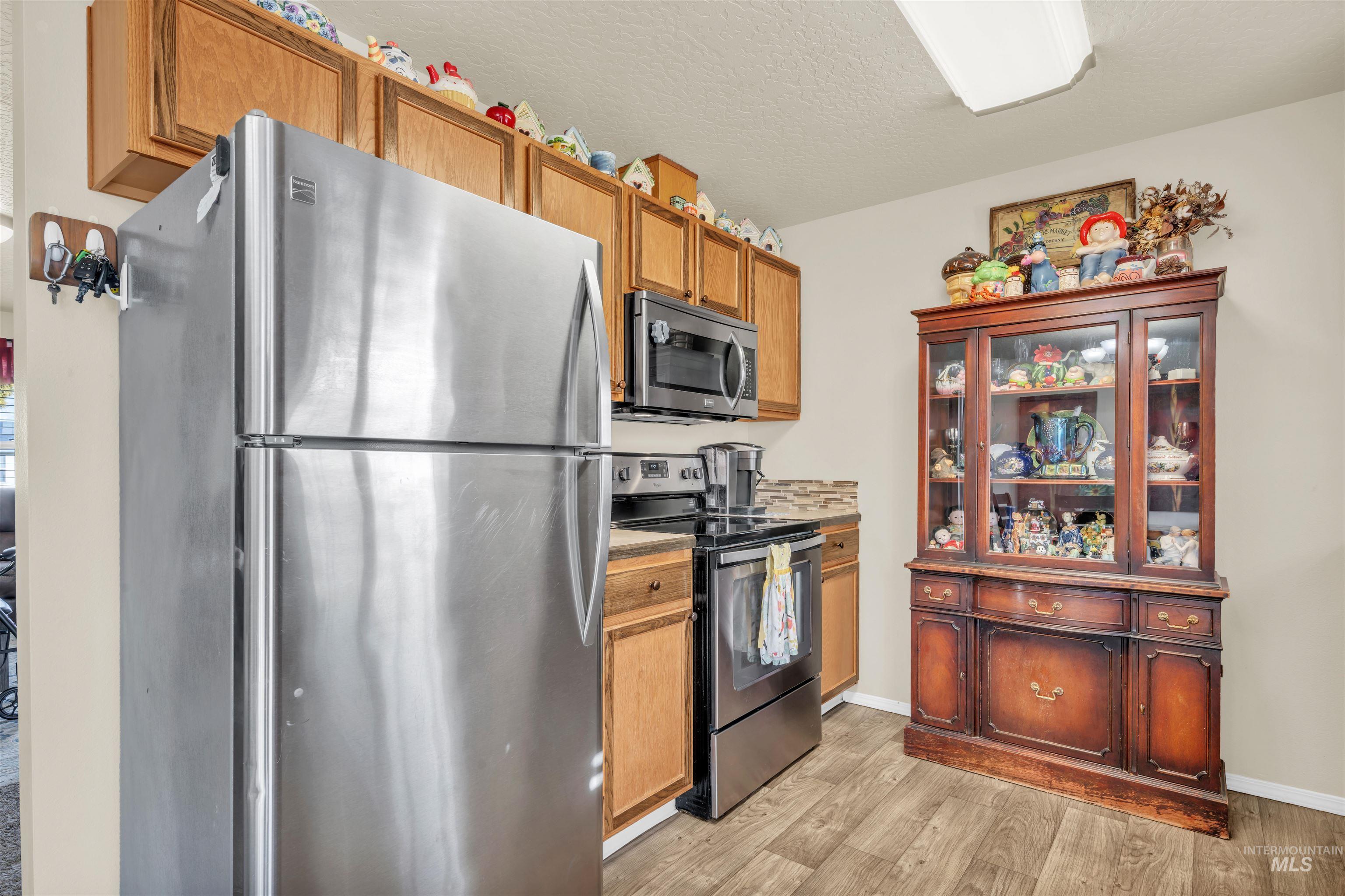 Kitchen with stainless steel appliances, light wood finished floors, a textured ceiling, light countertops, and glass insert cabinets