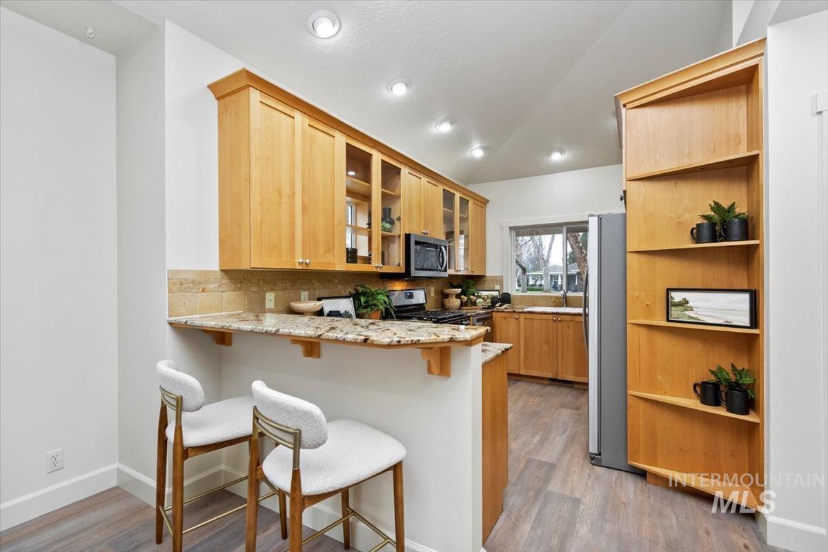 Kitchen with a peninsula, a kitchen bar, light stone countertops, open shelves, and recessed lighting