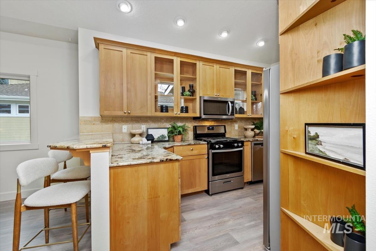 Kitchen featuring light stone countertops, stainless steel appliances, a breakfast bar area, a peninsula, and light brown cabinetry