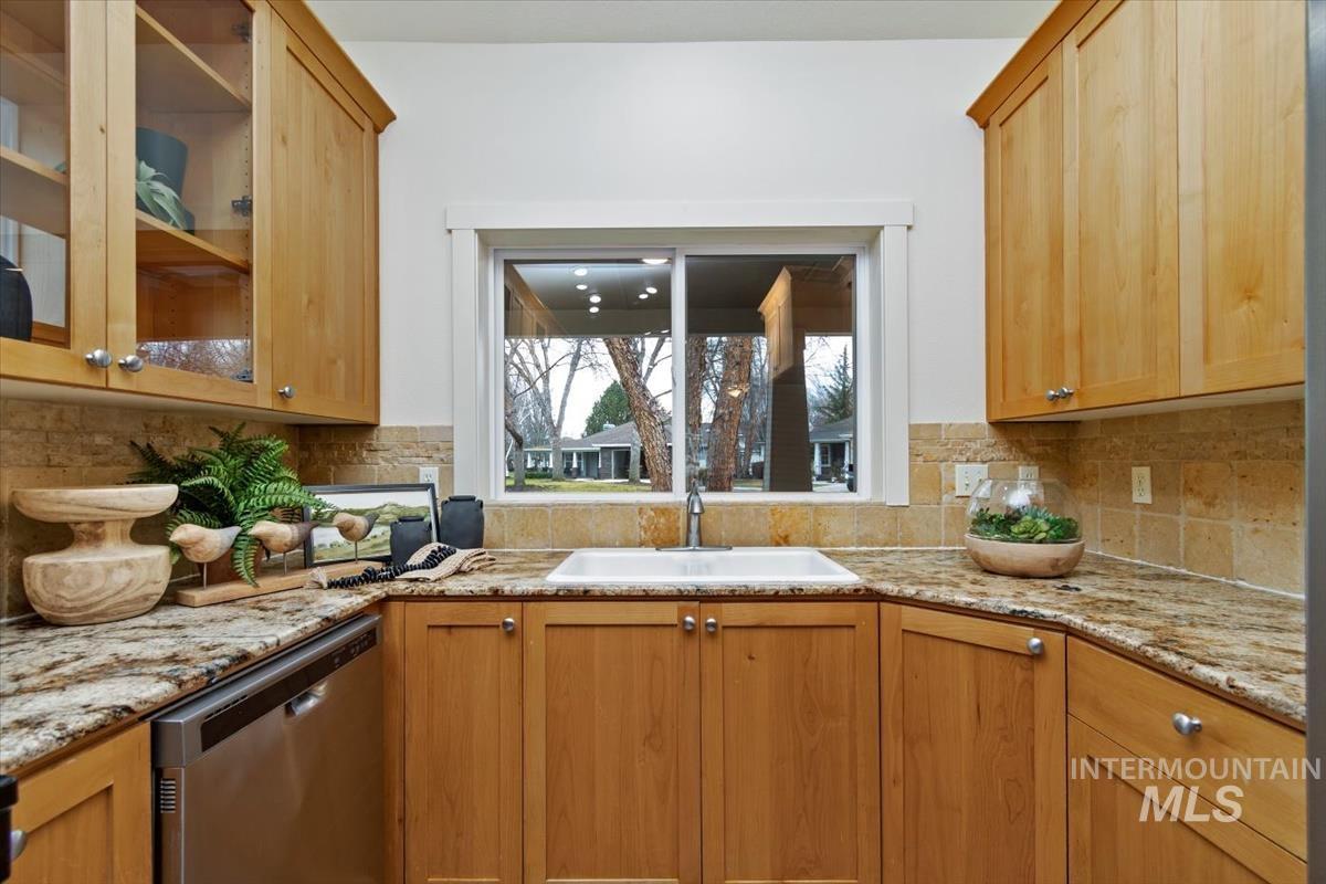 Kitchen featuring dishwasher, backsplash, and light stone countertops