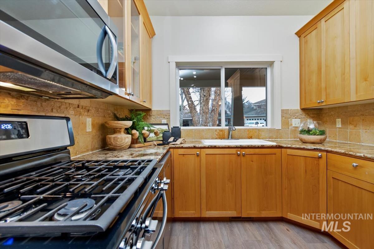 Kitchen with stainless steel appliances, light wood-style floors, light stone countertops, and backsplash
