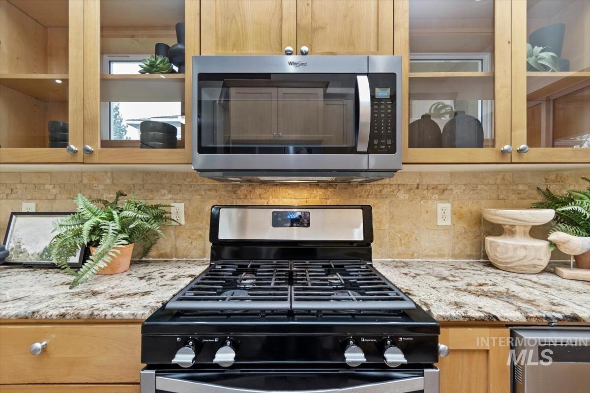 Kitchen with glass insert cabinets, stainless steel appliances, light-colored granite countertops, ample cabinetry, and tasteful backsplash