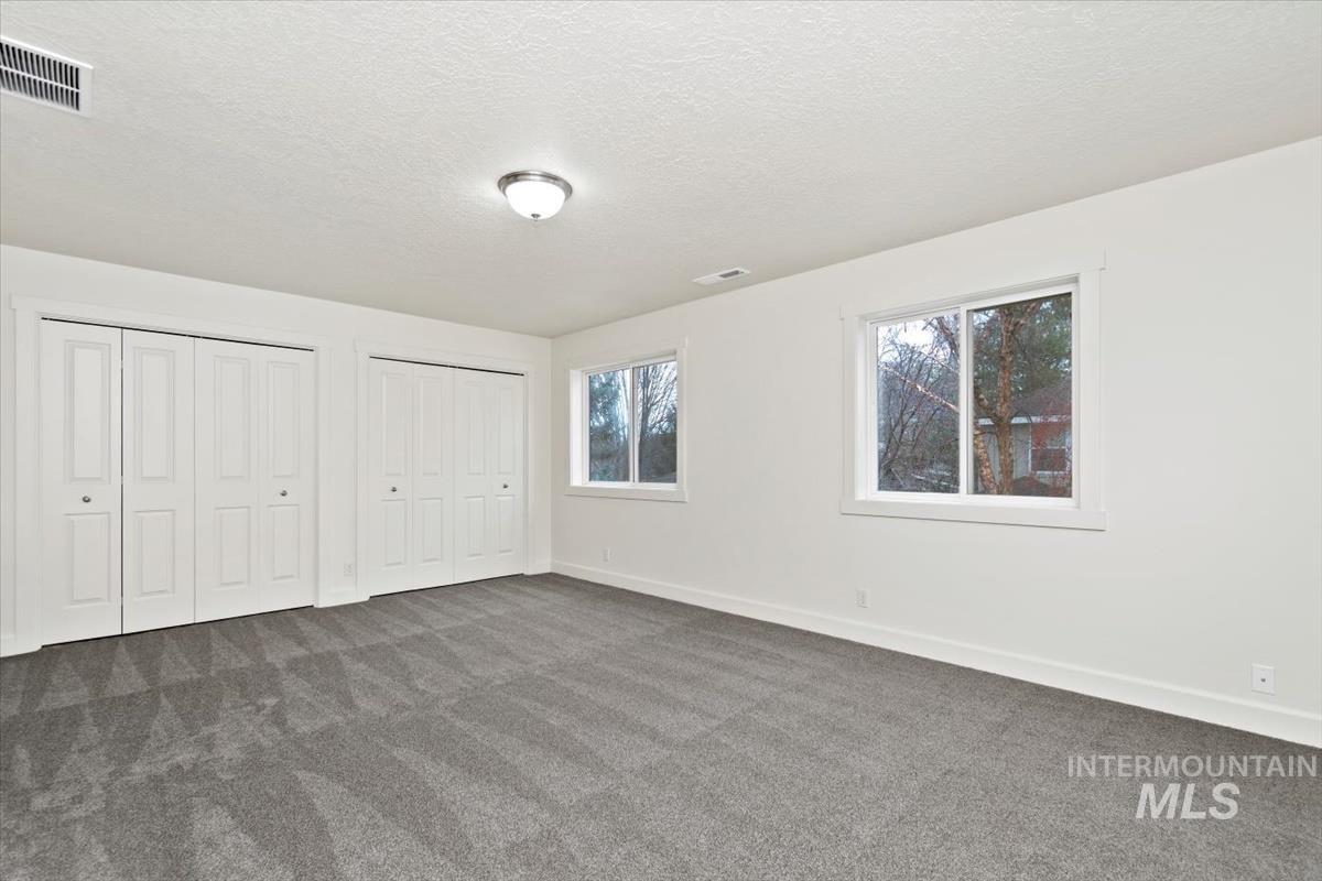 Unfurnished bedroom with multiple closets, new carpet, a textured ceiling, and multiple windows