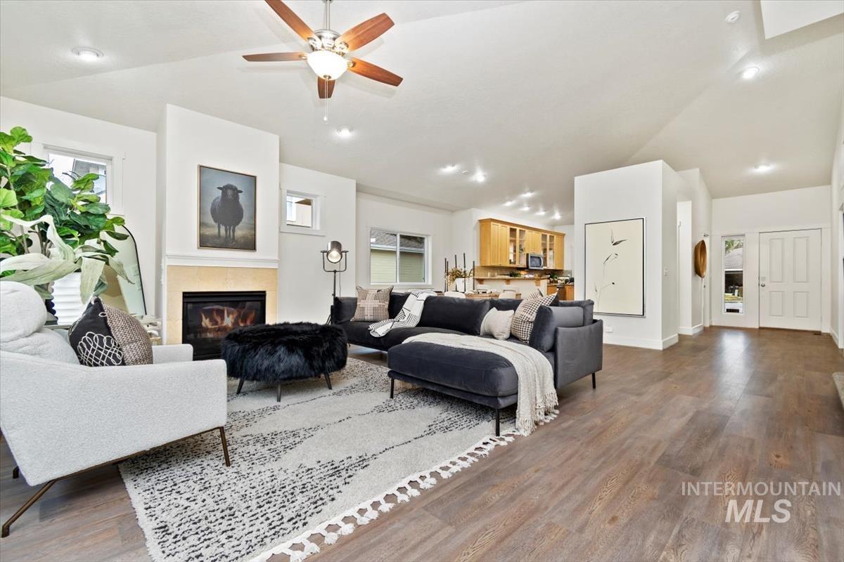 Great room with lofted ceiling, dark wood-style flooring, a glass covered fireplace, and a new ceiling fan