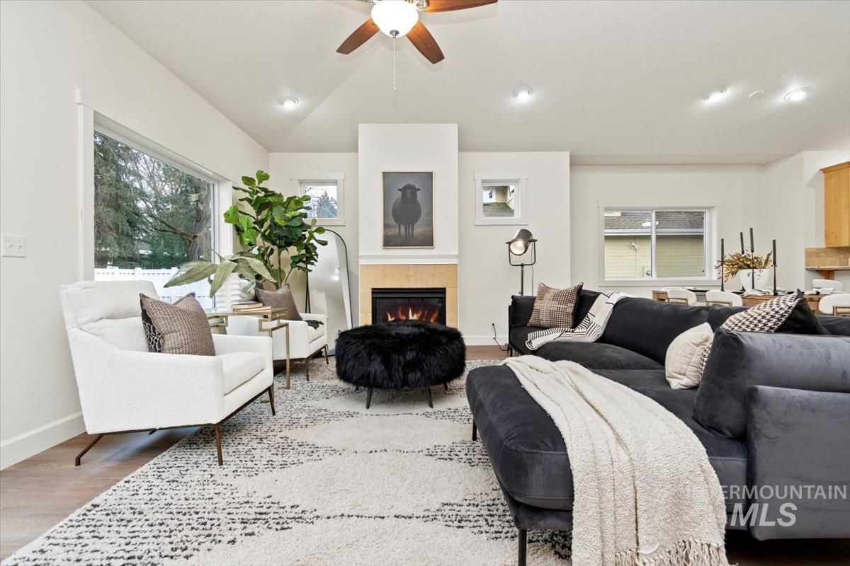 Living area with vaulted ceiling, wood finished floors, a tile fireplace, a ceiling fan, and recessed lighting
