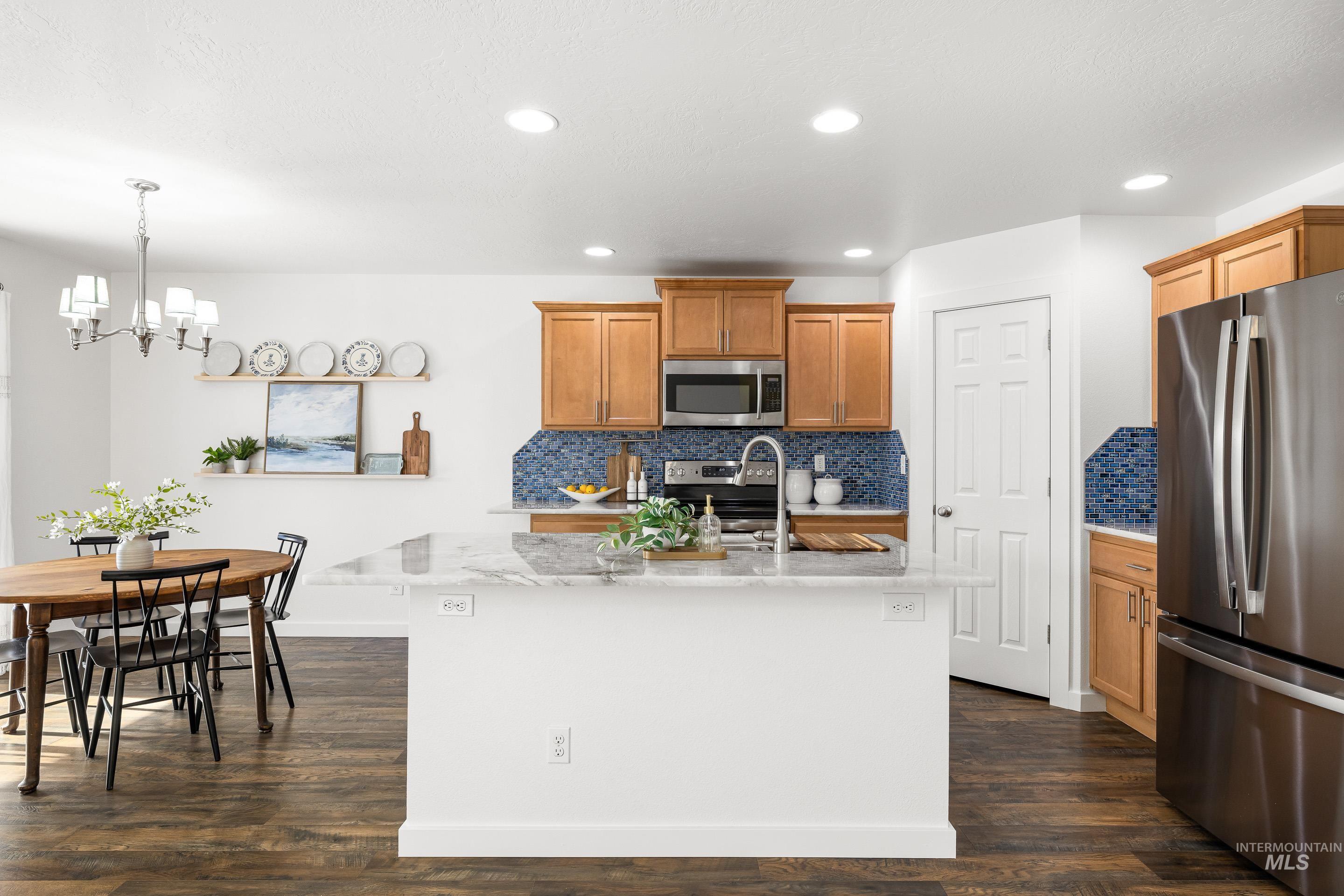 Kitchen with stainless steel appliances, tasteful backsplash, light stone countertops, dark wood-style floors, and decorative light fixtures