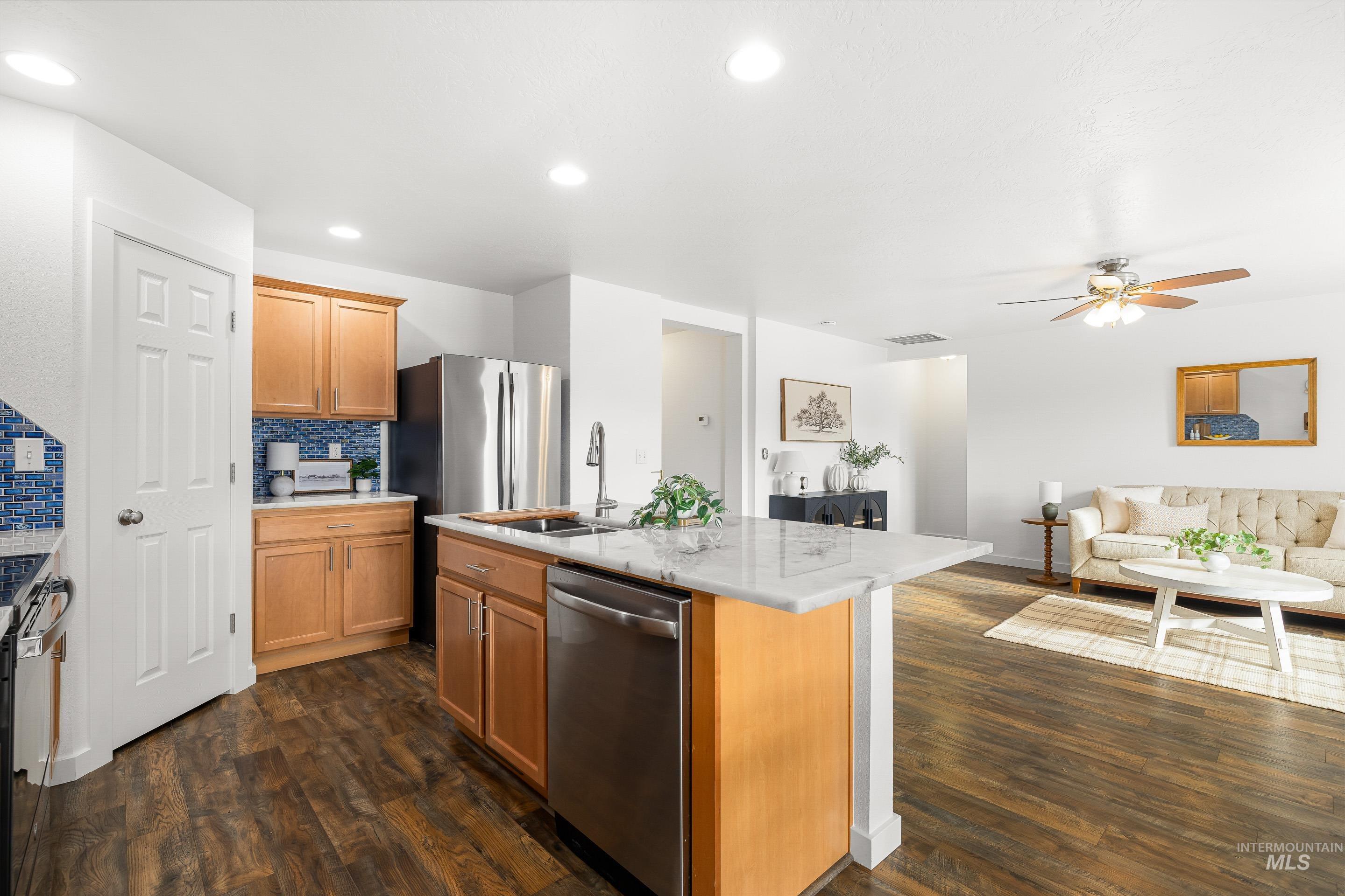 Kitchen with backsplash, appliances with stainless steel finishes, an island with sink, open floor plan, and dark wood-type flooring