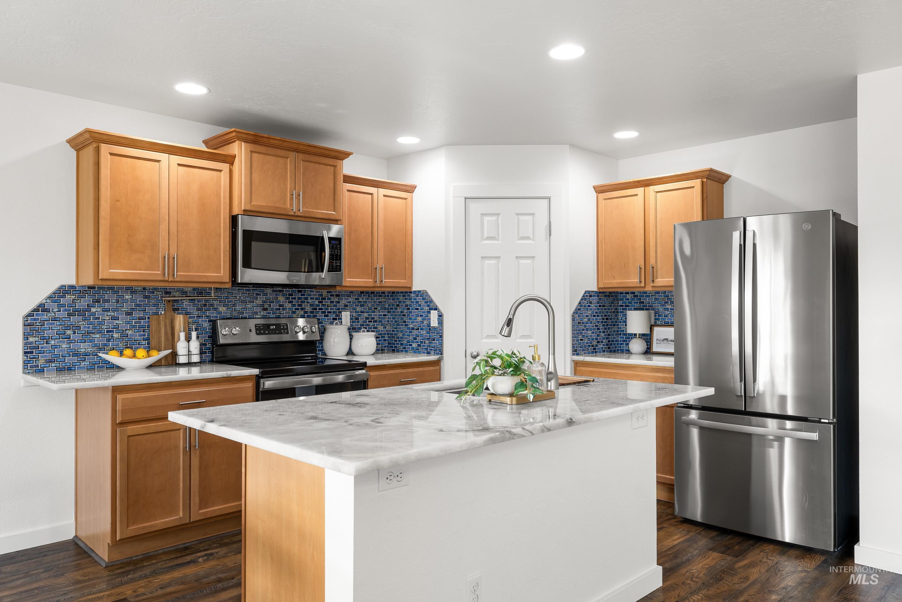 Kitchen with appliances with stainless steel finishes, light stone counters, backsplash, a kitchen island with sink, and recessed lighting