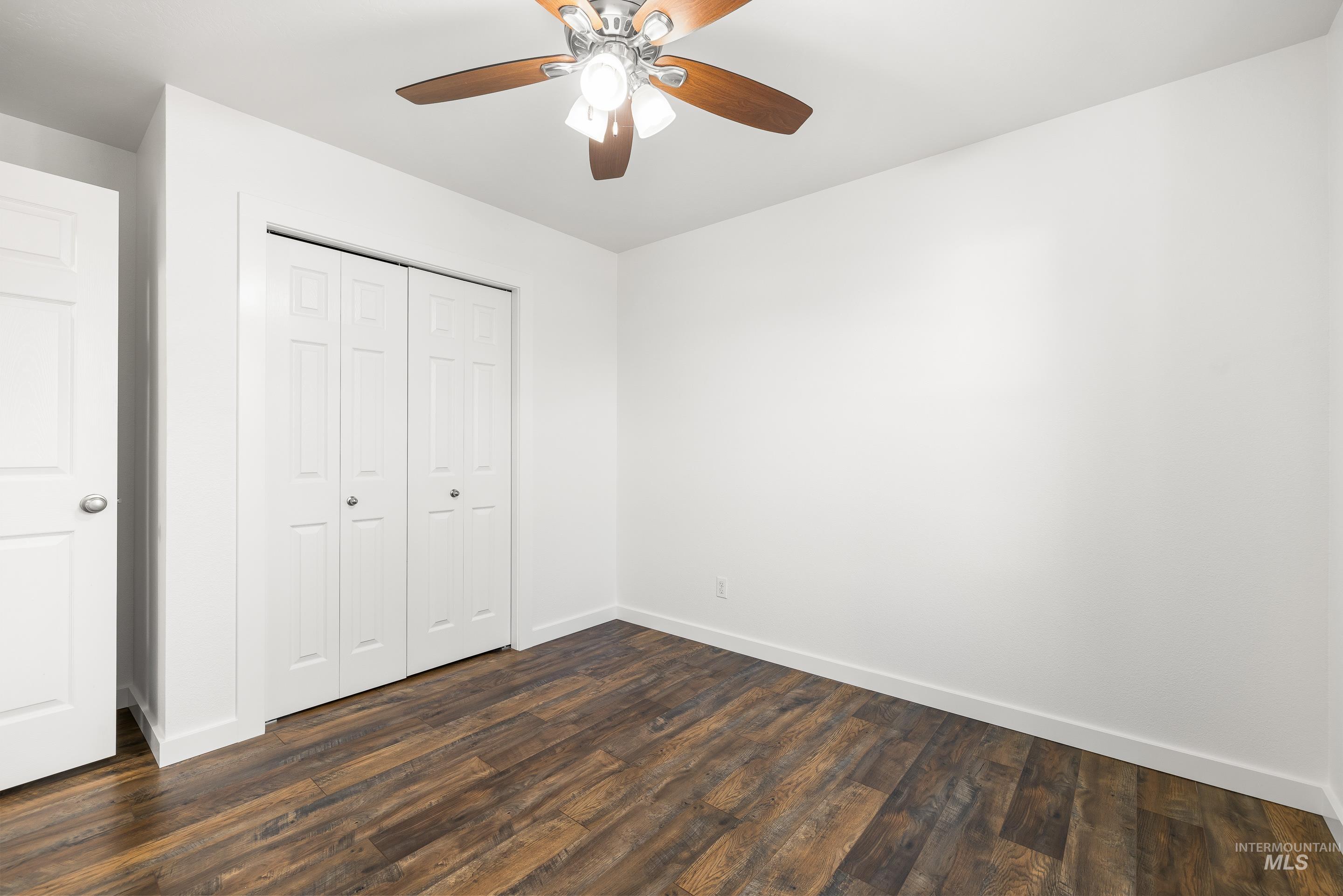 Unfurnished bedroom featuring a closet, dark wood-style floors, and ceiling fan