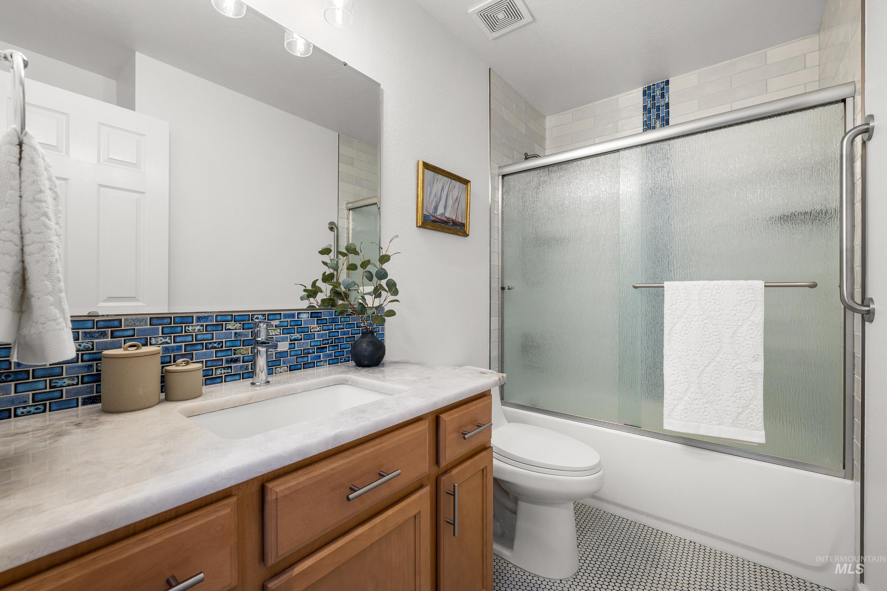 Bathroom with vanity, shower / bath combination with glass door, and decorative backsplash