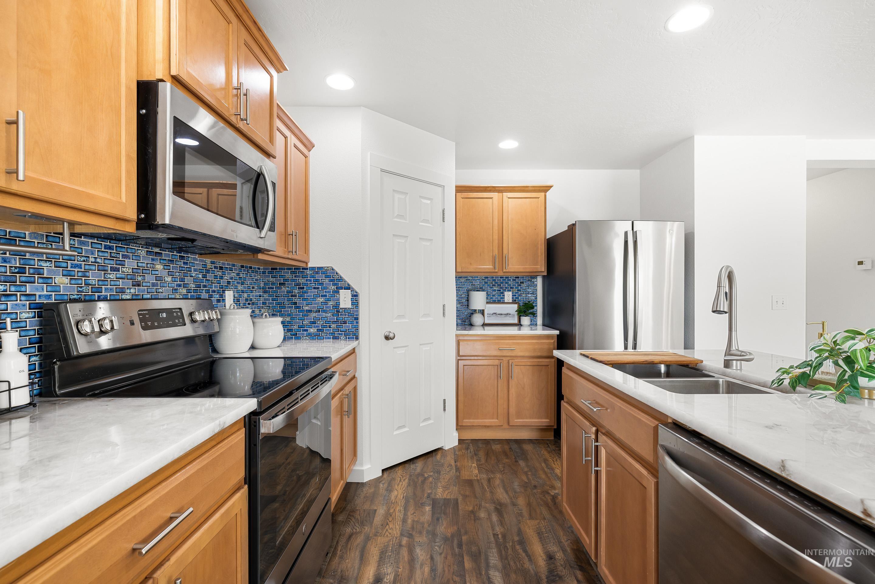 Kitchen with appliances with stainless steel finishes, light stone counters, dark wood-style flooring, tasteful backsplash, and recessed lighting