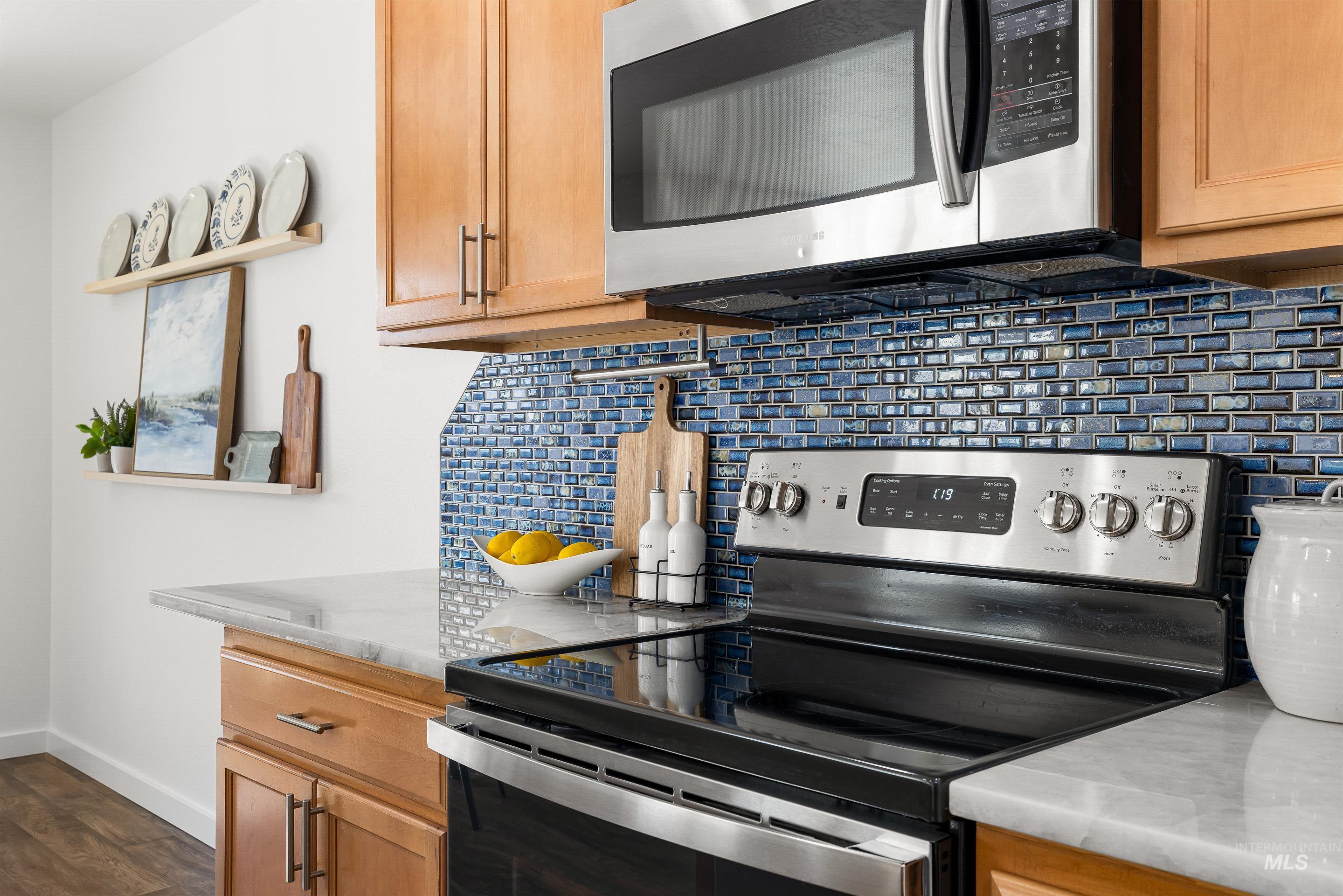 Kitchen featuring stainless steel appliances, decorative backsplash, light stone countertops, and brown cabinets