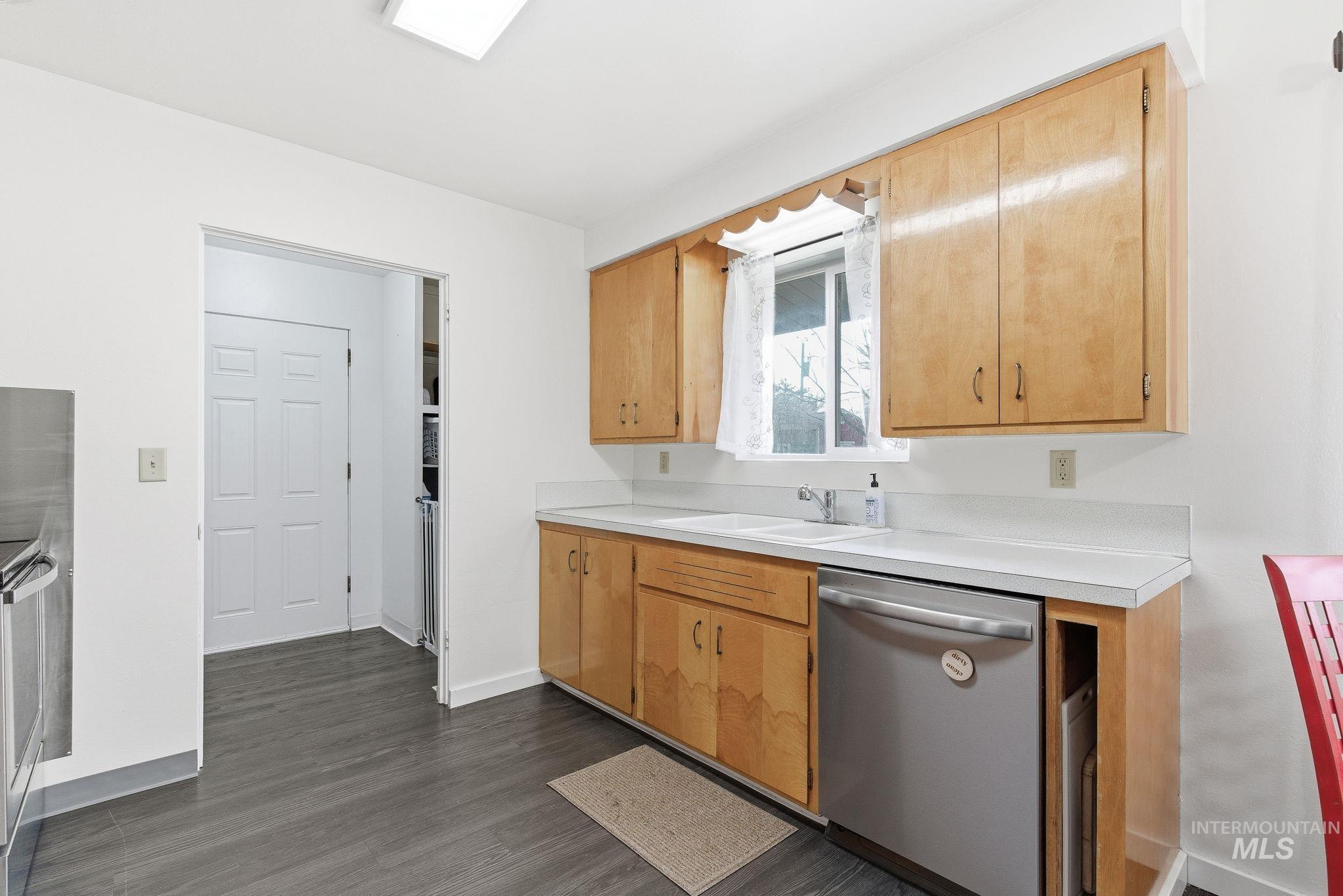 Kitchen featuring light countertops, appliances with stainless steel finishes, dark wood-style flooring, and light brown cabinetry