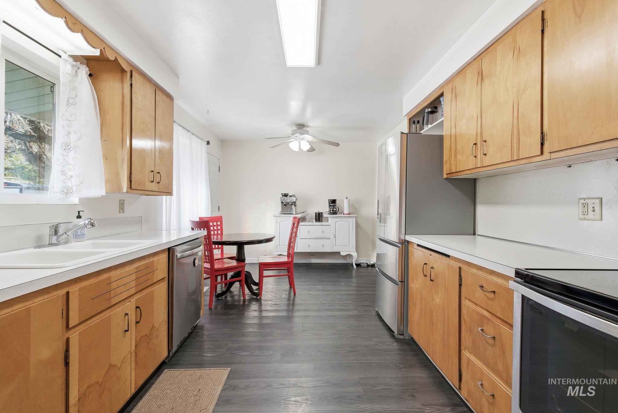Kitchen featuring light countertops, dark wood-type flooring, appliances with stainless steel finishes, and a ceiling fan