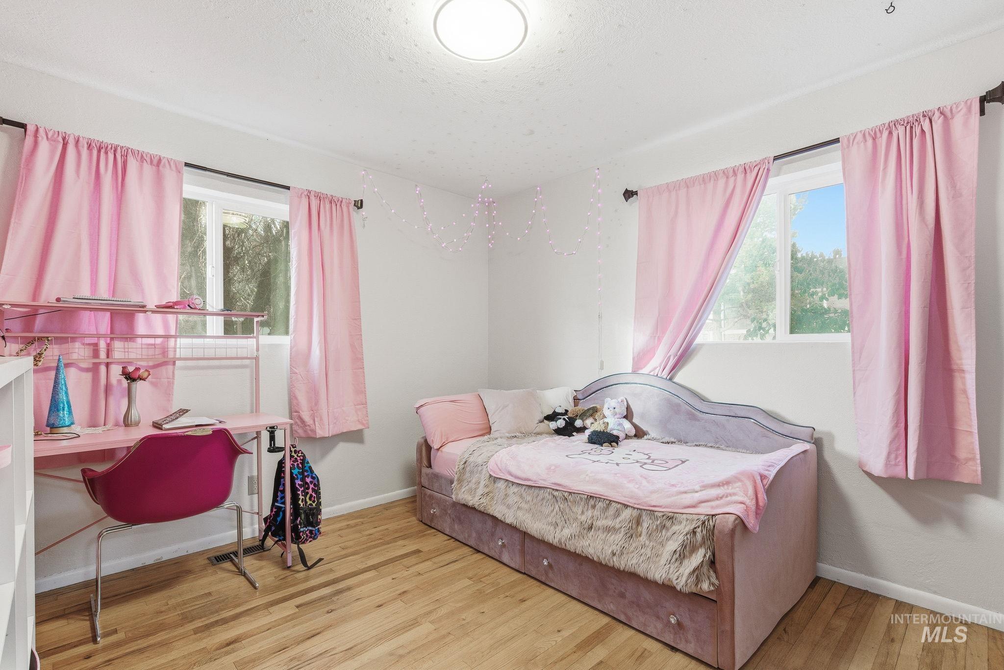 Bedroom featuring multiple windows, light wood-style floors, and a desk