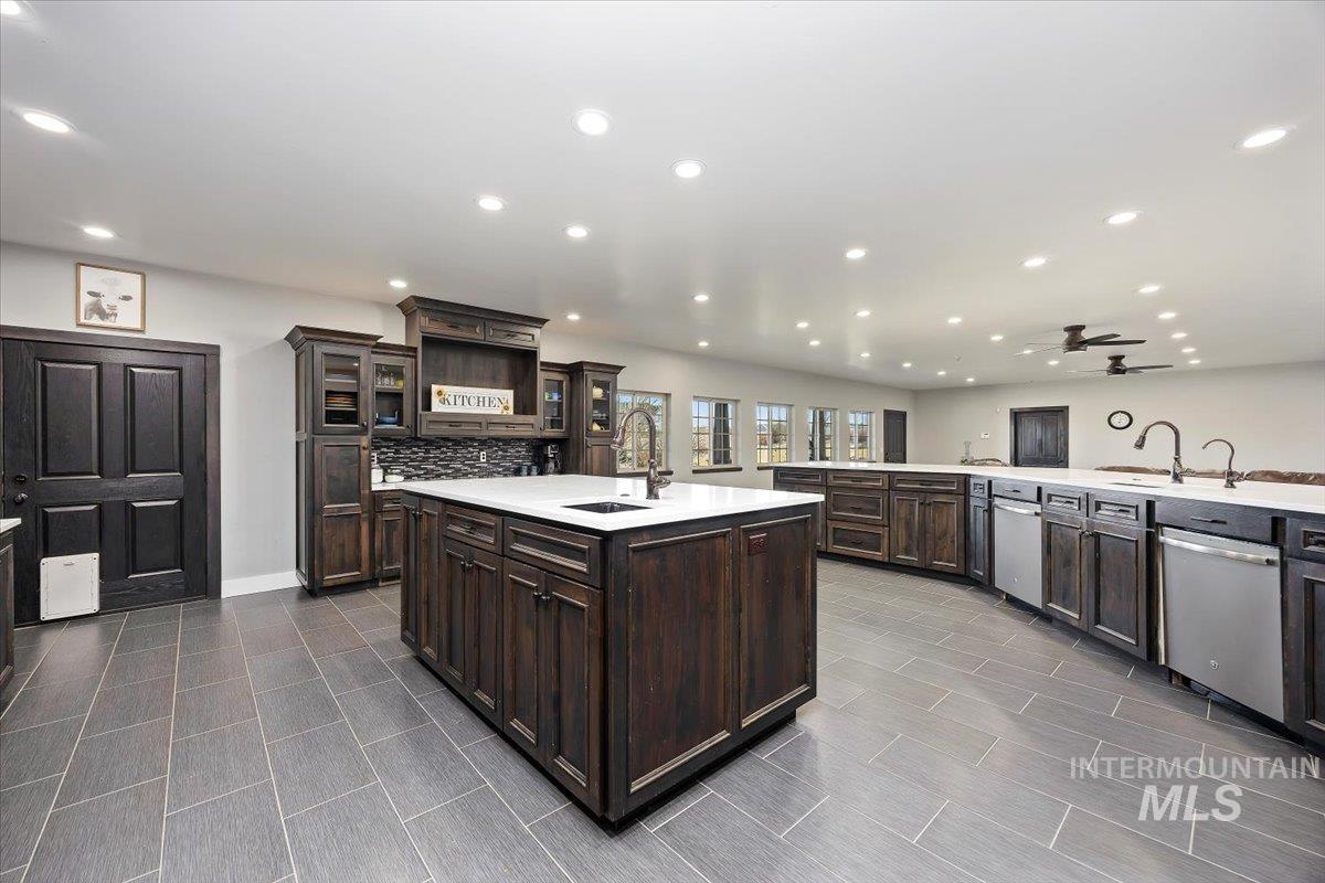 Kitchen with a large island, glass insert cabinets, dark brown cabinetry, light stone countertops, and recessed lighting