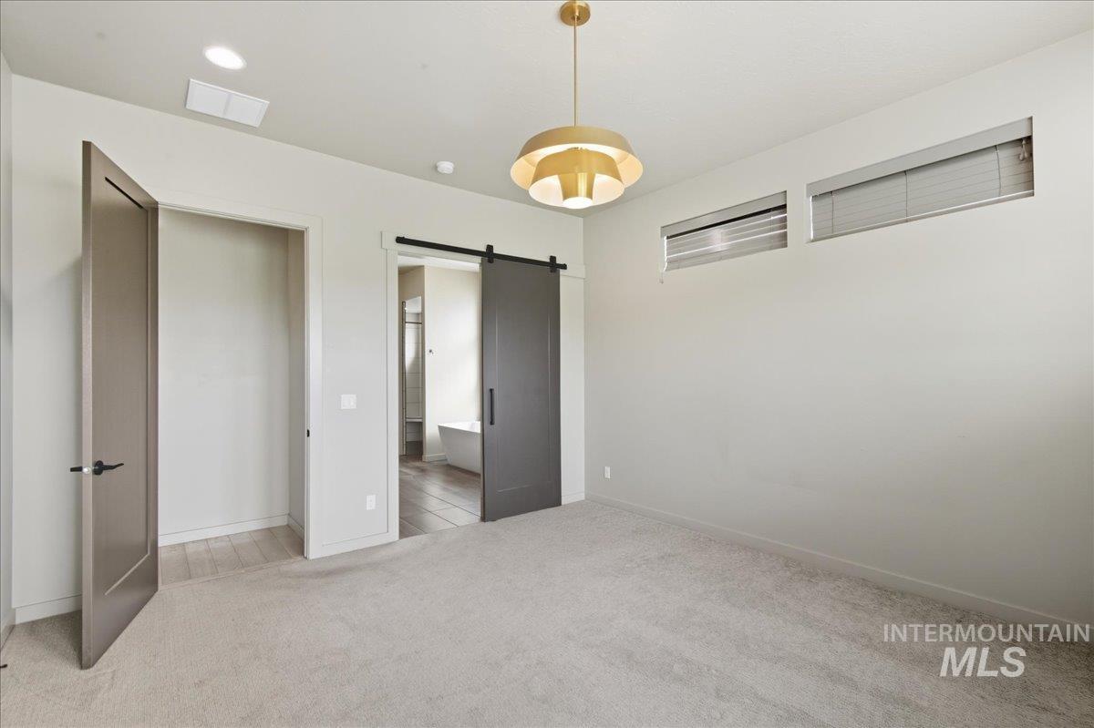 Unfurnished bedroom featuring a barn door, light colored carpet, connected bathroom, and recessed lighting