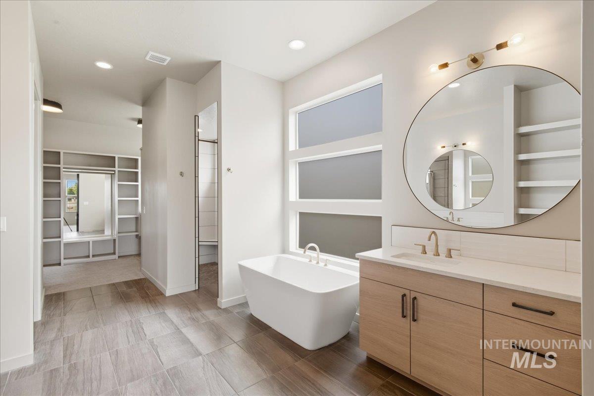 Full bath with a spacious closet, a freestanding bath, vanity, and recessed lighting