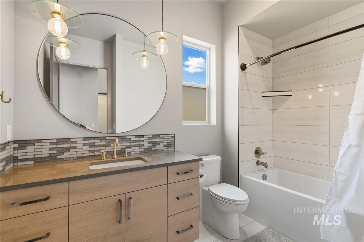 Bathroom featuring shower / bath combo with shower curtain, vanity, tasteful backsplash, and light tile patterned flooring