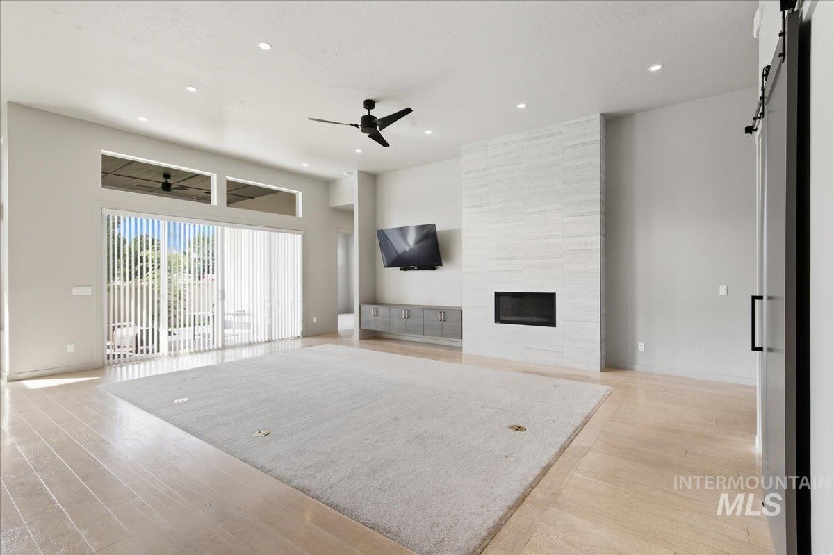 Unfurnished living room featuring a barn door, light wood-type flooring, a large fireplace, recessed lighting, and a ceiling fan