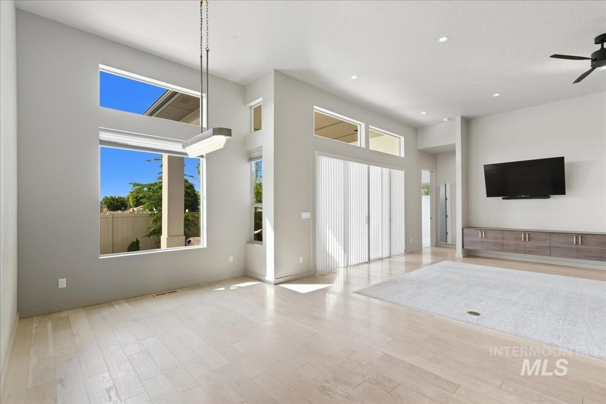 Unfurnished living room featuring light wood finished floors, a high ceiling, a ceiling fan, and recessed lighting