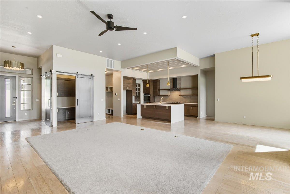Unfurnished living room featuring a barn door, light wood-type flooring, ceiling fan, recessed lighting, and a chandelier