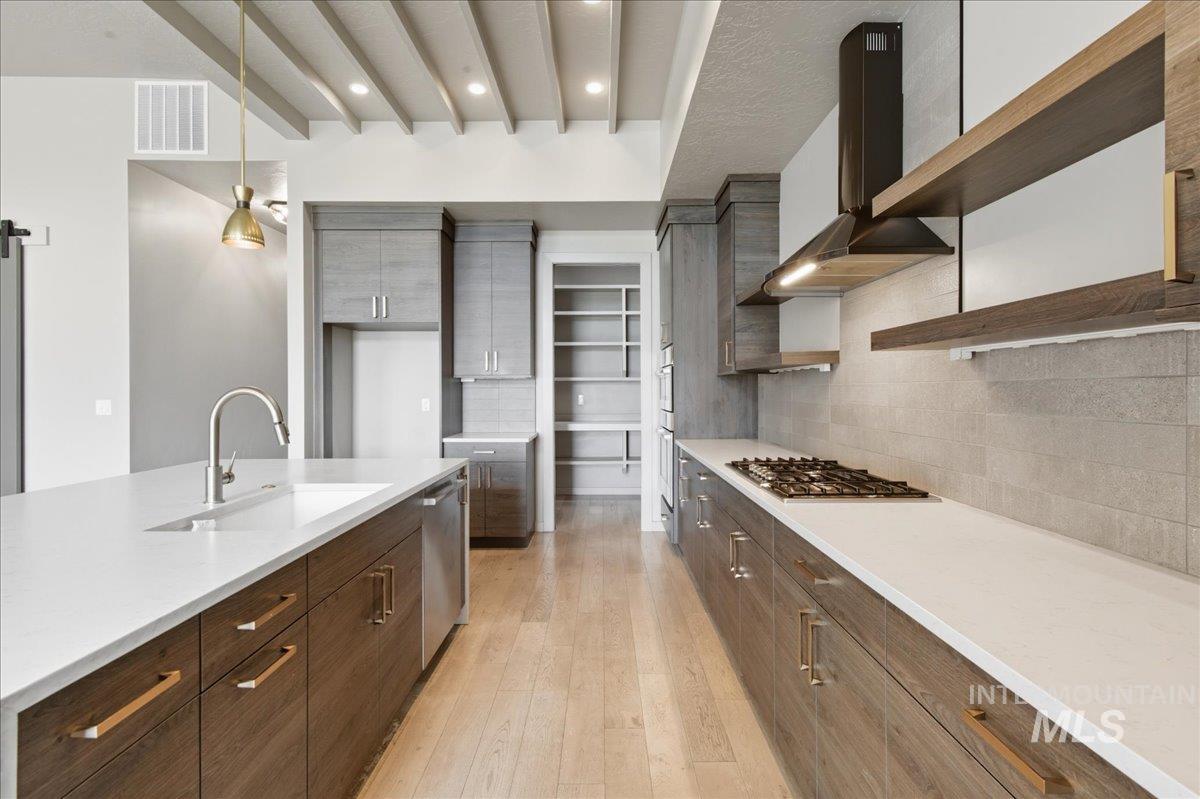 Kitchen featuring open shelves, backsplash, pendant lighting, wall chimney exhaust hood, and light wood-type flooring