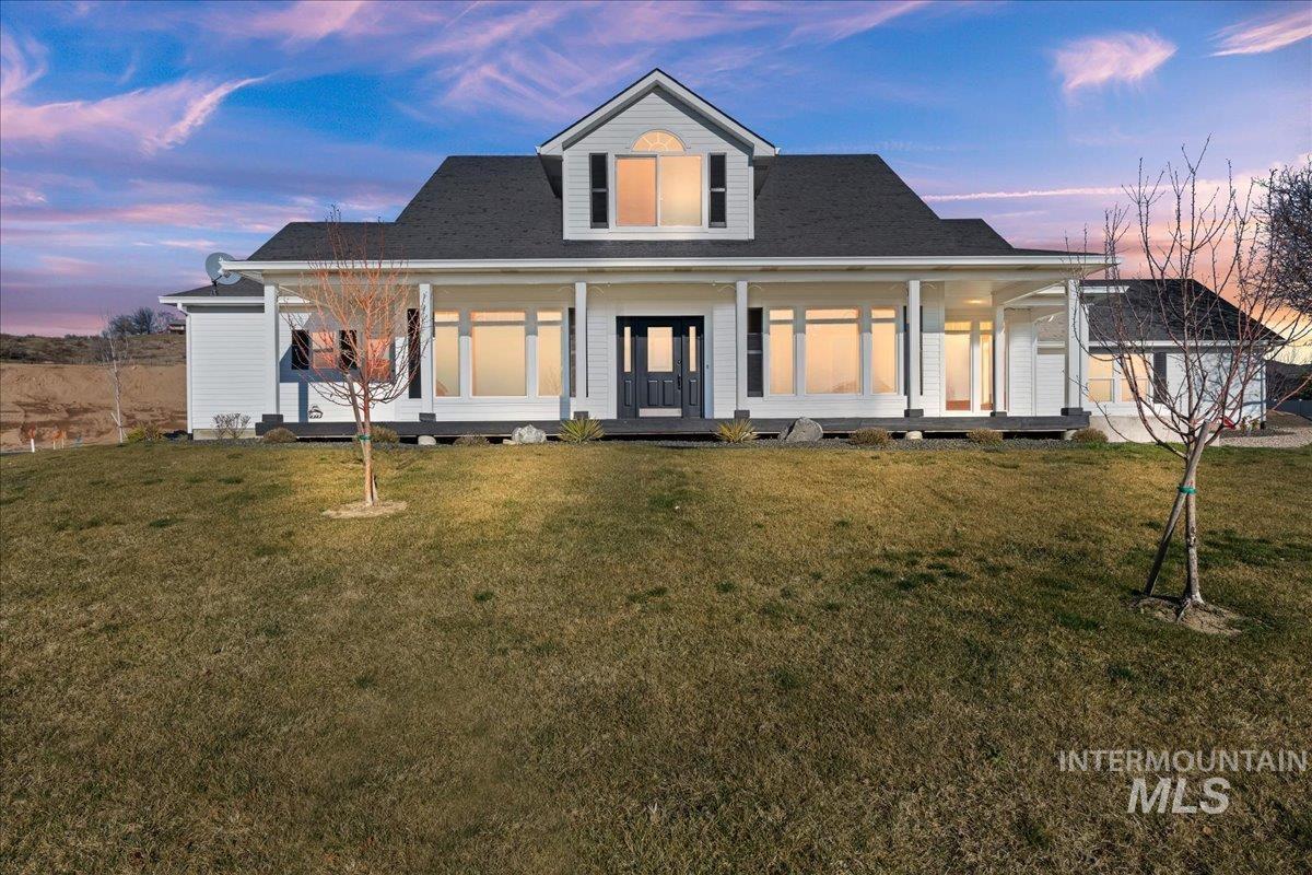 Back of house at dusk with a porch, a yard, and a shingled roof