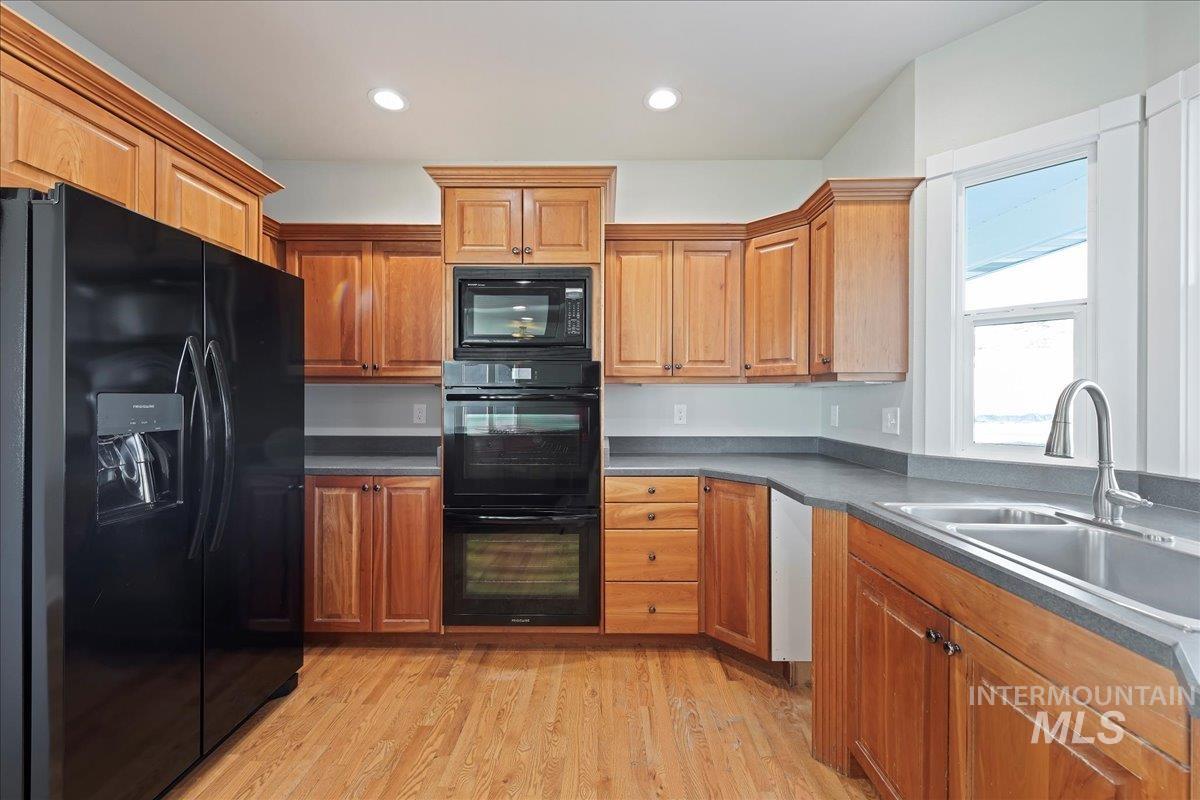Kitchen featuring black appliances, dark countertops, recessed lighting, light wood-style flooring, and brown cabinets