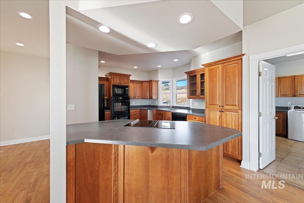 Kitchen with glass insert cabinets, washer / clothes dryer, light wood-style floors, and dark countertops
