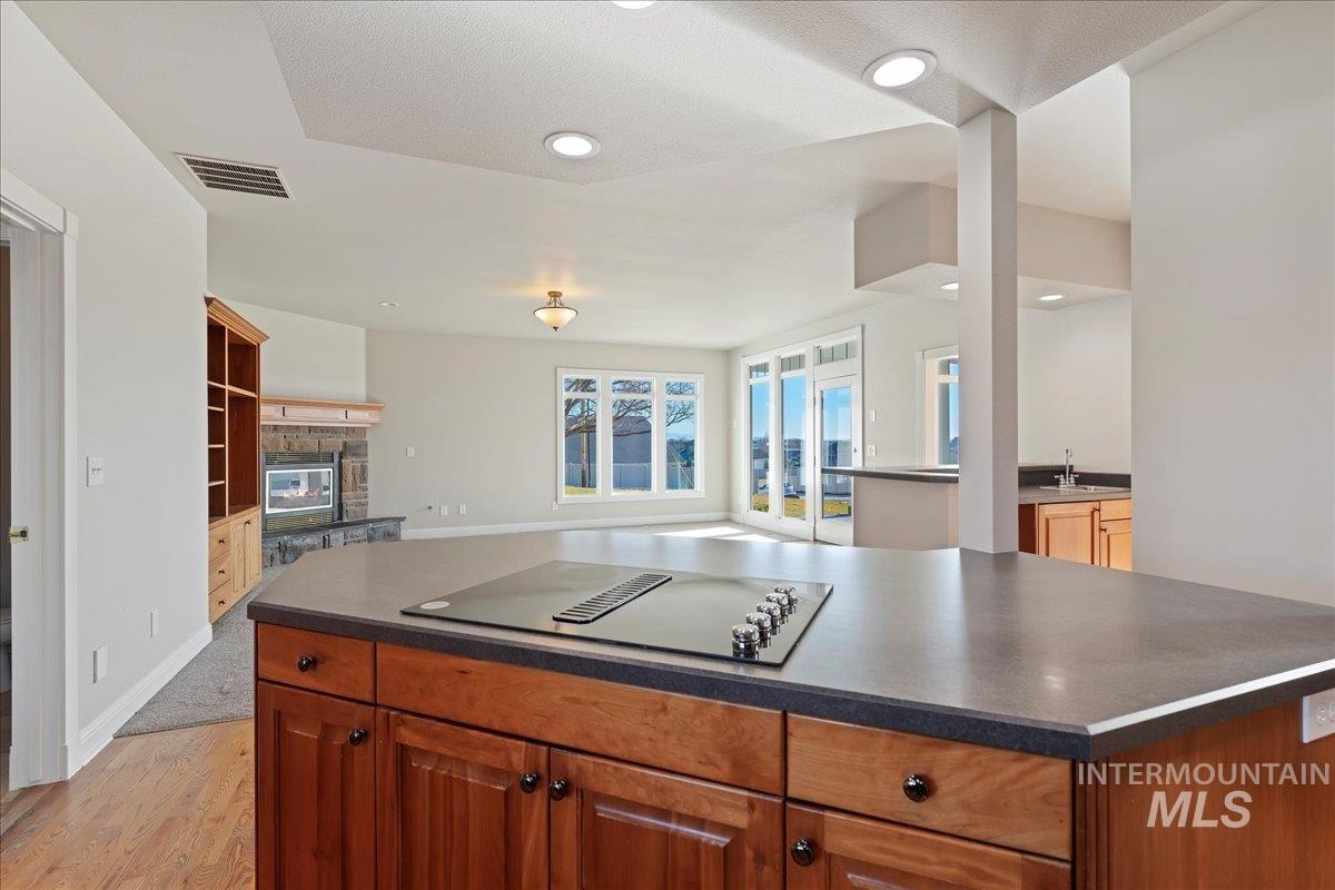 Kitchen featuring dark countertops, a fireplace, brown cabinets, black electric cooktop, and open floor plan