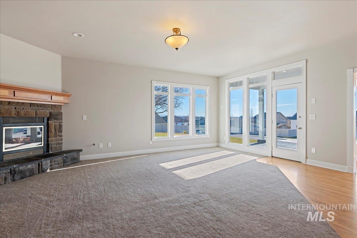 Unfurnished living room with a stone fireplace and baseboards
