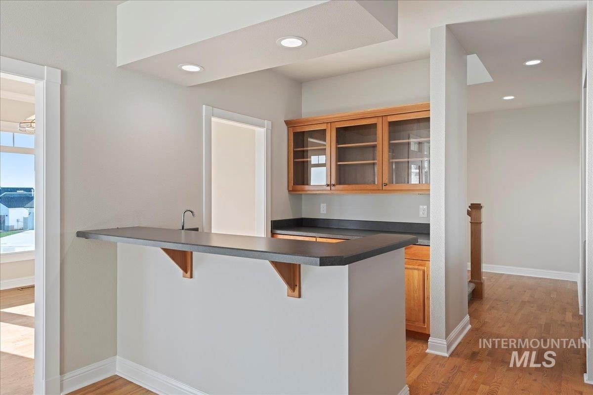 Kitchen featuring a kitchen bar, glass insert cabinets, dark countertops, light wood finished floors, and recessed lighting
