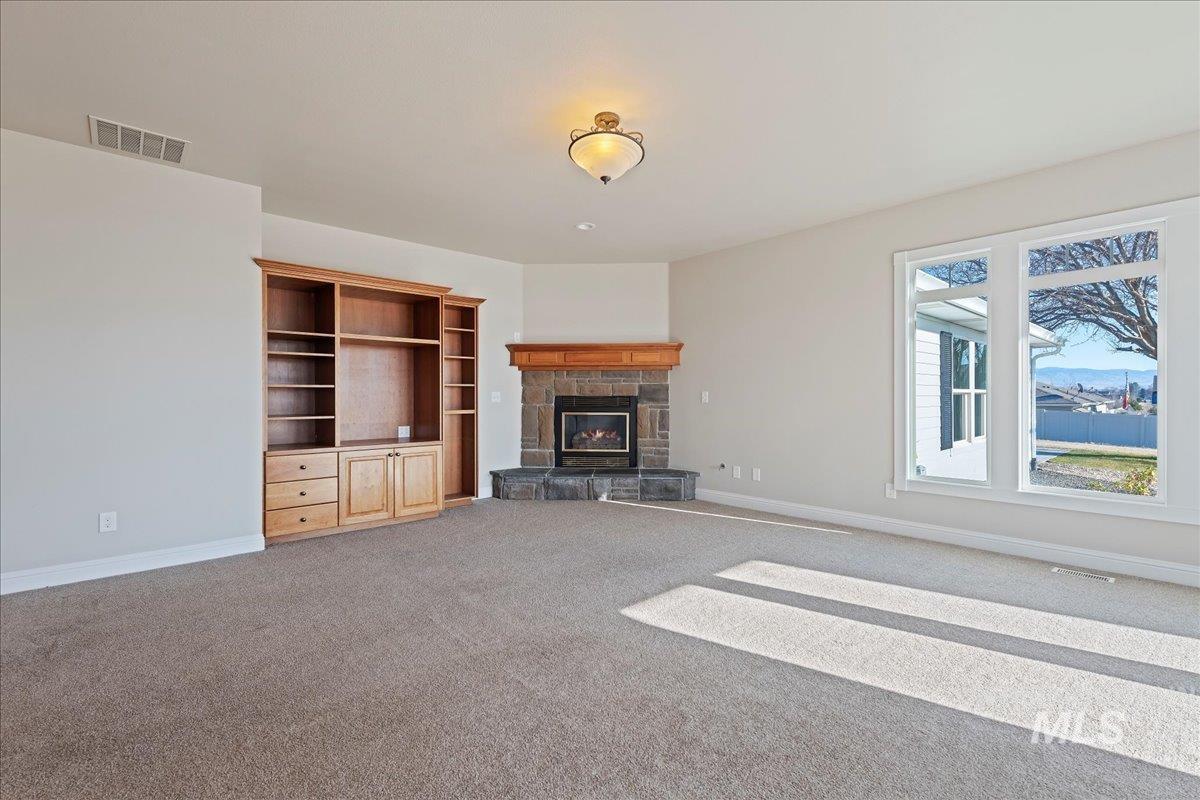 Unfurnished living room featuring a stone fireplace and light carpet