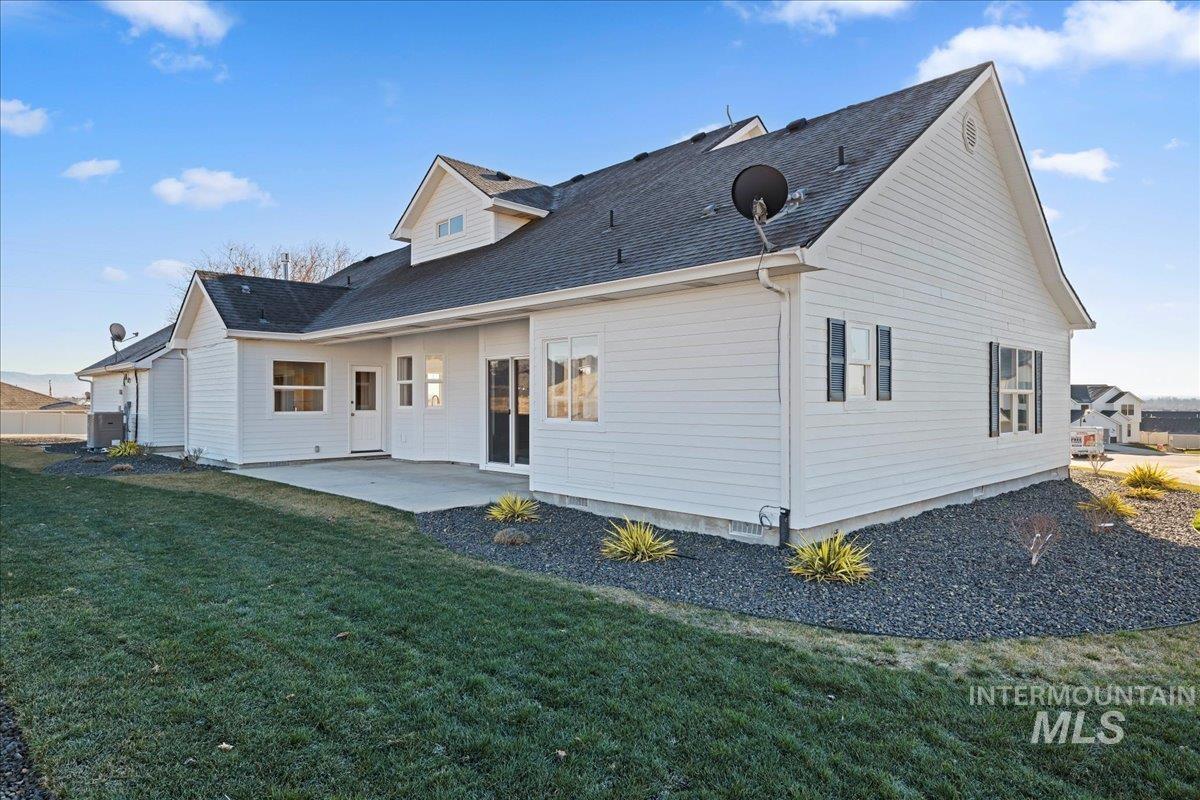 Rear view of house featuring a patio, a lawn, and roof with shingles