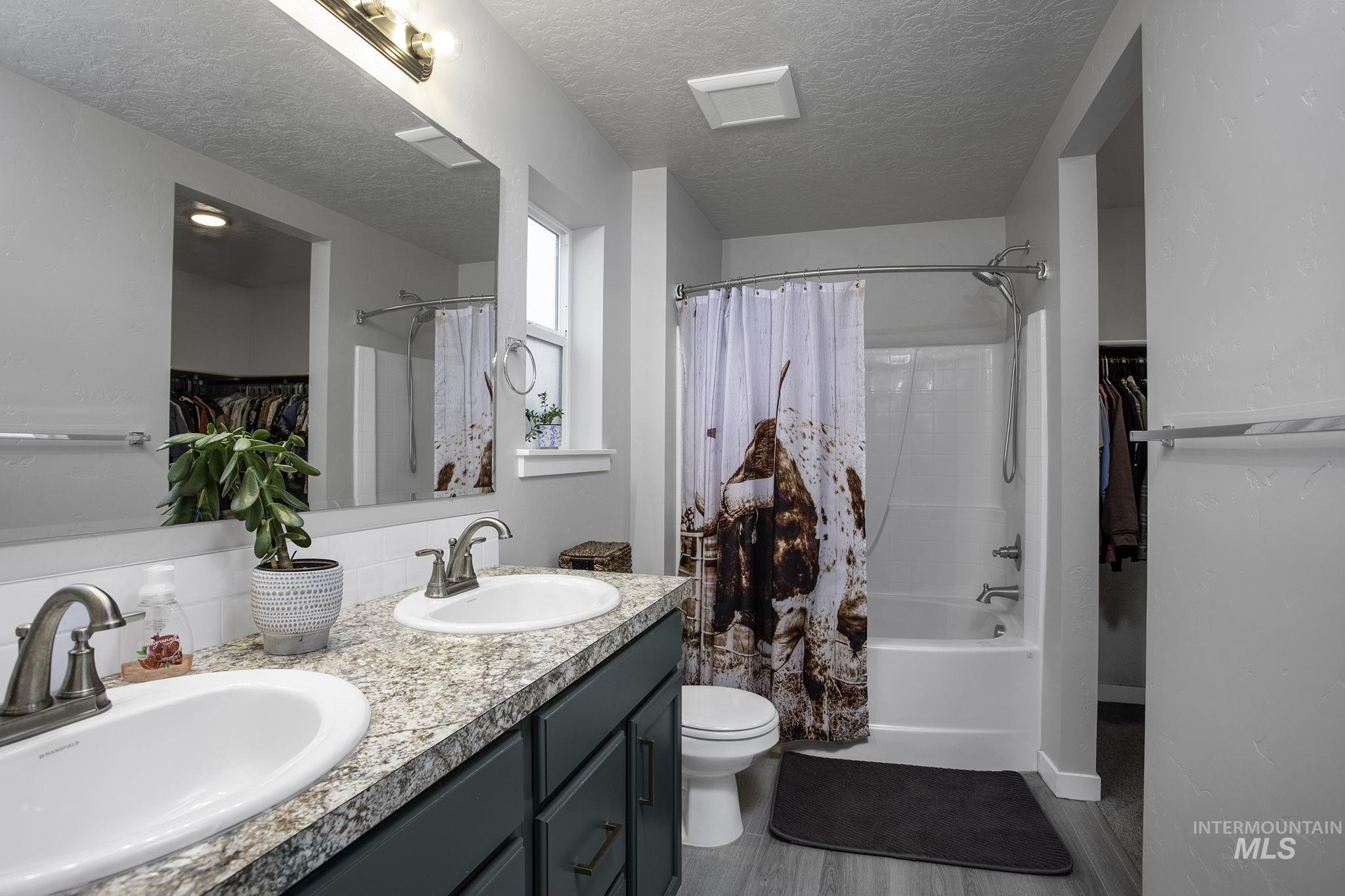 Bathroom featuring a spacious closet, double vanity, shower / tub combo, a textured ceiling, and dark wood-style flooring