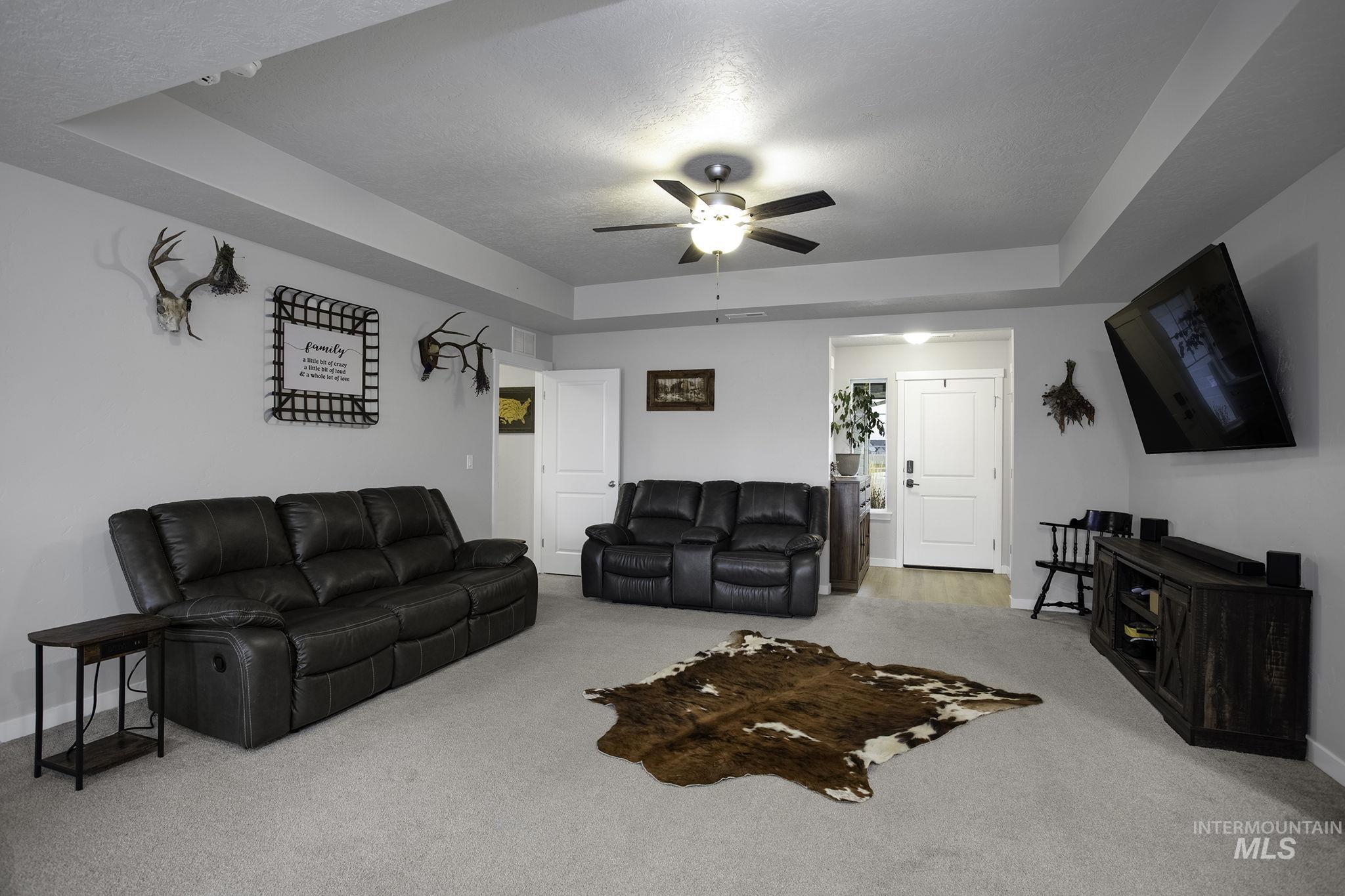 Living area featuring a tray ceiling, light carpet, a textured ceiling, and ceiling fan