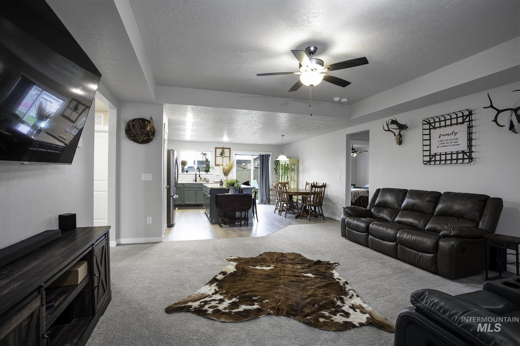Living area with a textured ceiling, ceiling fan, a raised ceiling, and light carpet