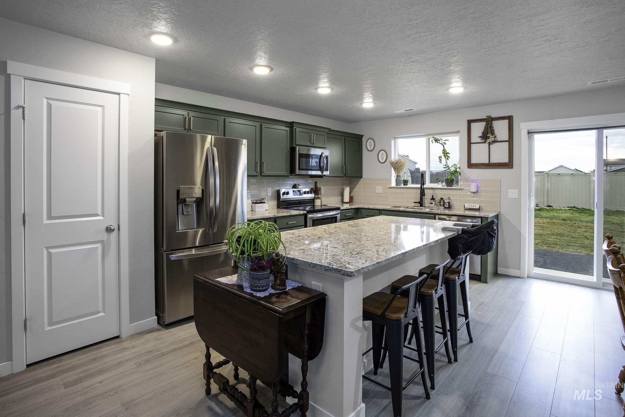 Kitchen featuring appliances with stainless steel finishes, a center island, light stone counters, a breakfast bar, and backsplash