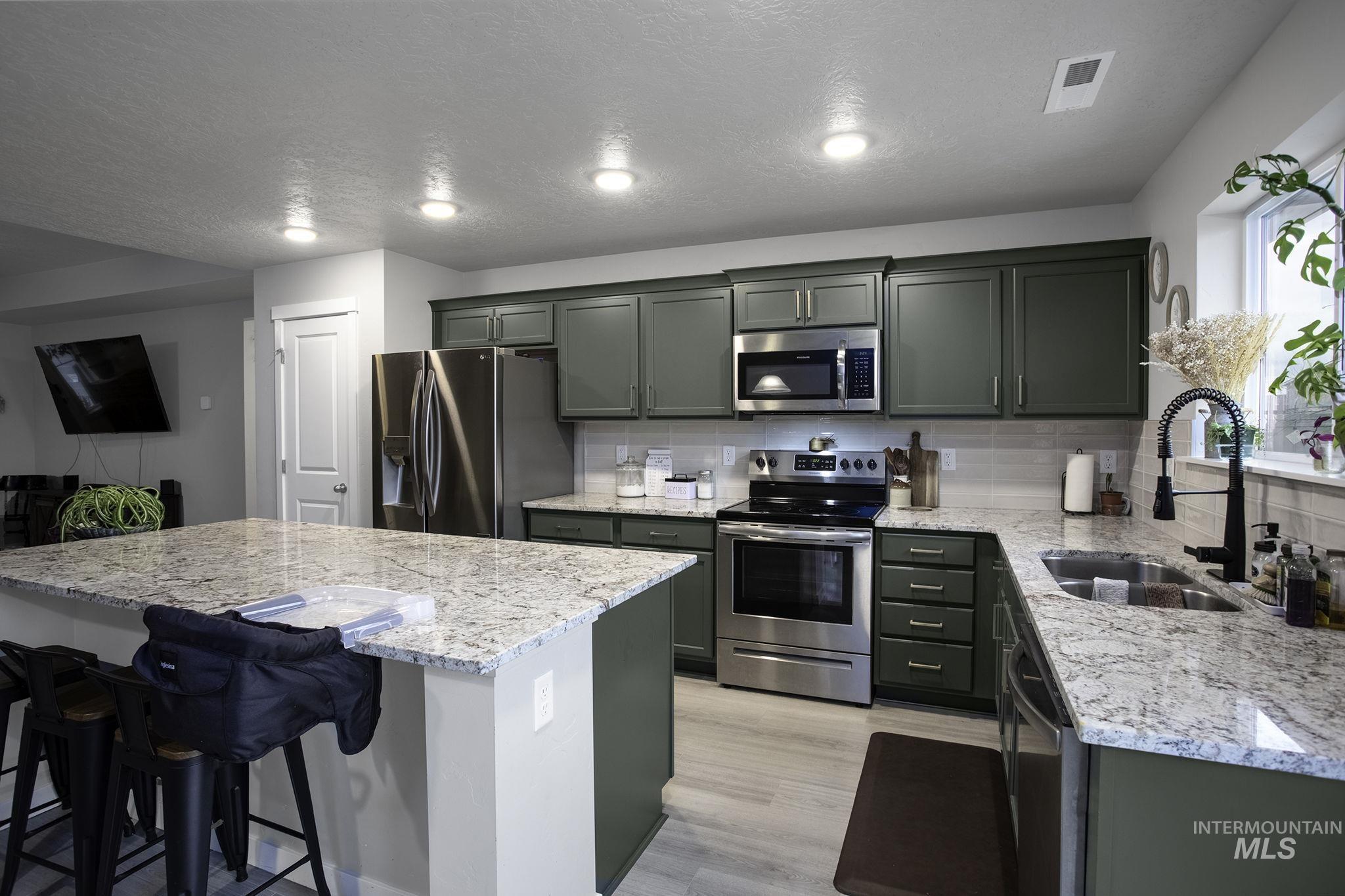 Kitchen featuring stainless steel appliances, light stone countertops, a kitchen bar, light wood finished floors, and a kitchen island