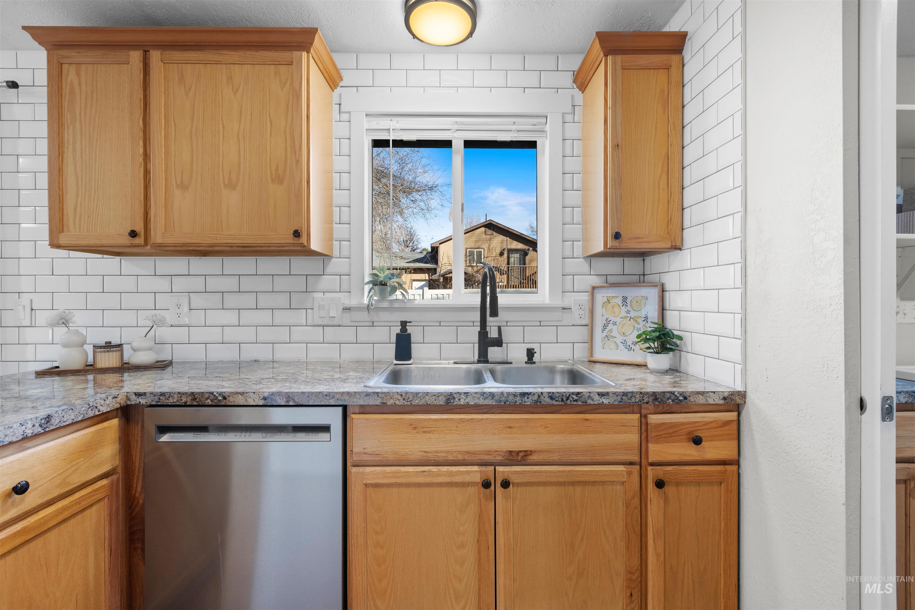 Kitchen with stainless steel dishwasher, backsplash, and light brown cabinets